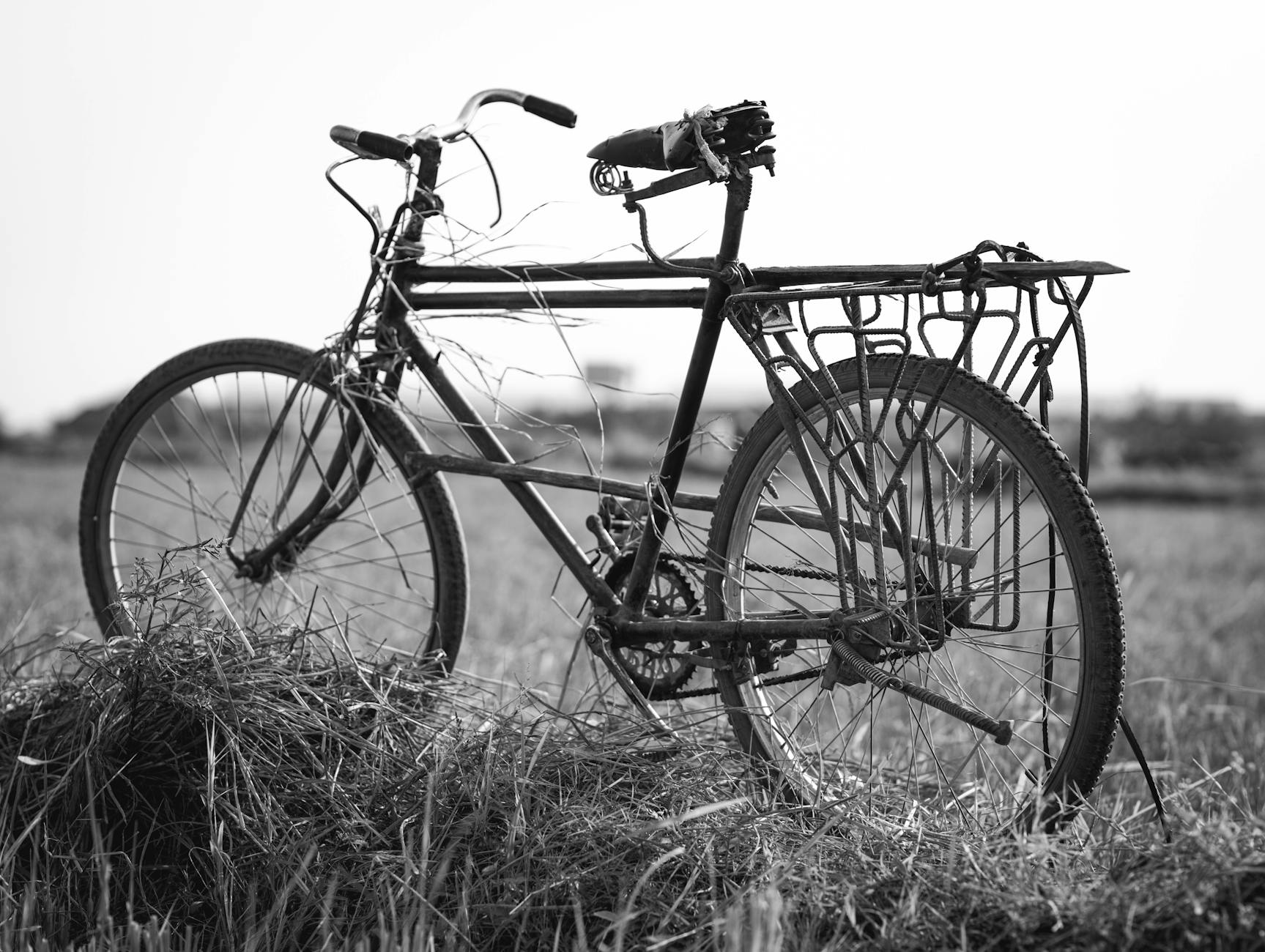 Black and white photo of a vintage bicycle in a rural field in Burundi, highlighting simplicity.
