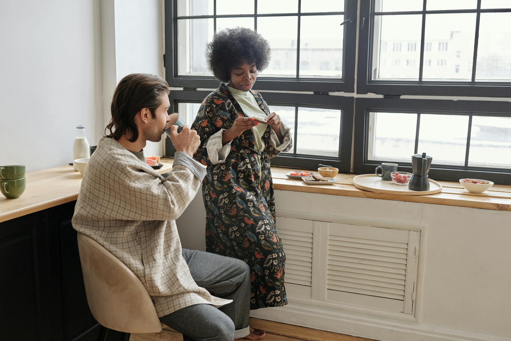 A relaxed morning scene with a couple having breakfast and coffee by a sunny window.