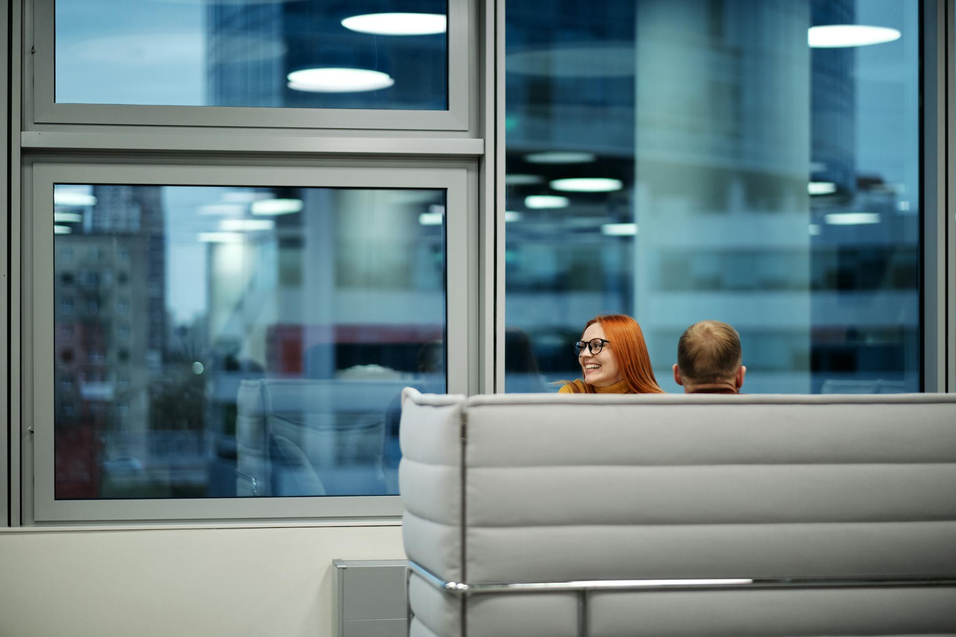 Colleagues enjoying a casual discussion in a spacious office lounge with large windows.