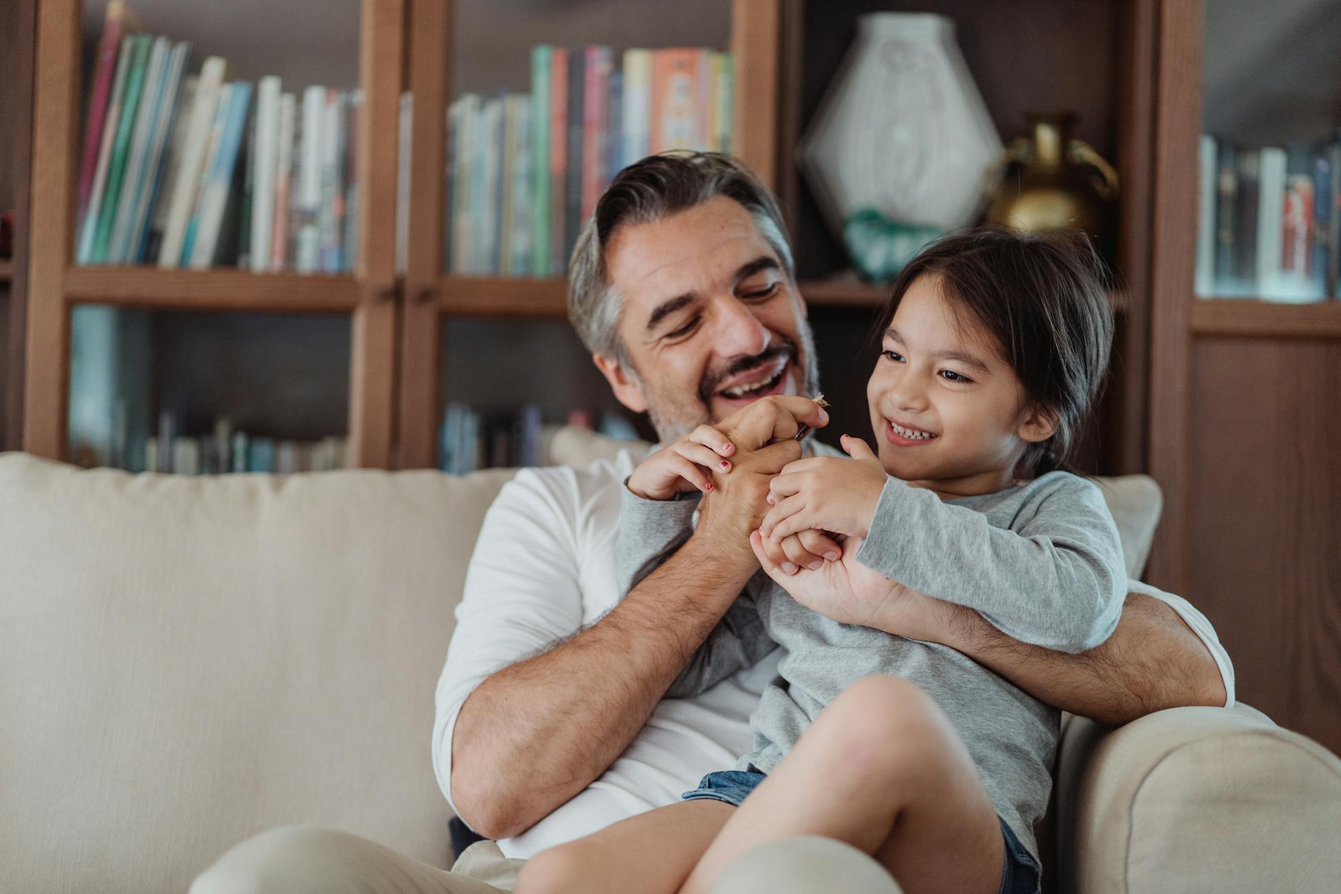 A loving father and daughter share a joyful moment on the couch, indoors.