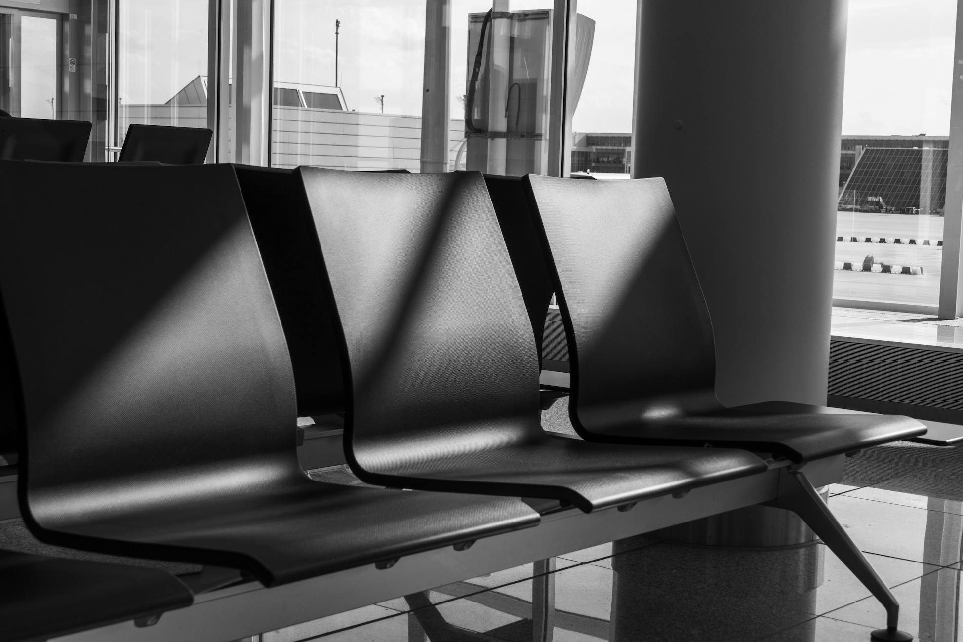 Minimalist black and white photo showcasing empty chairs in an airport terminal.
