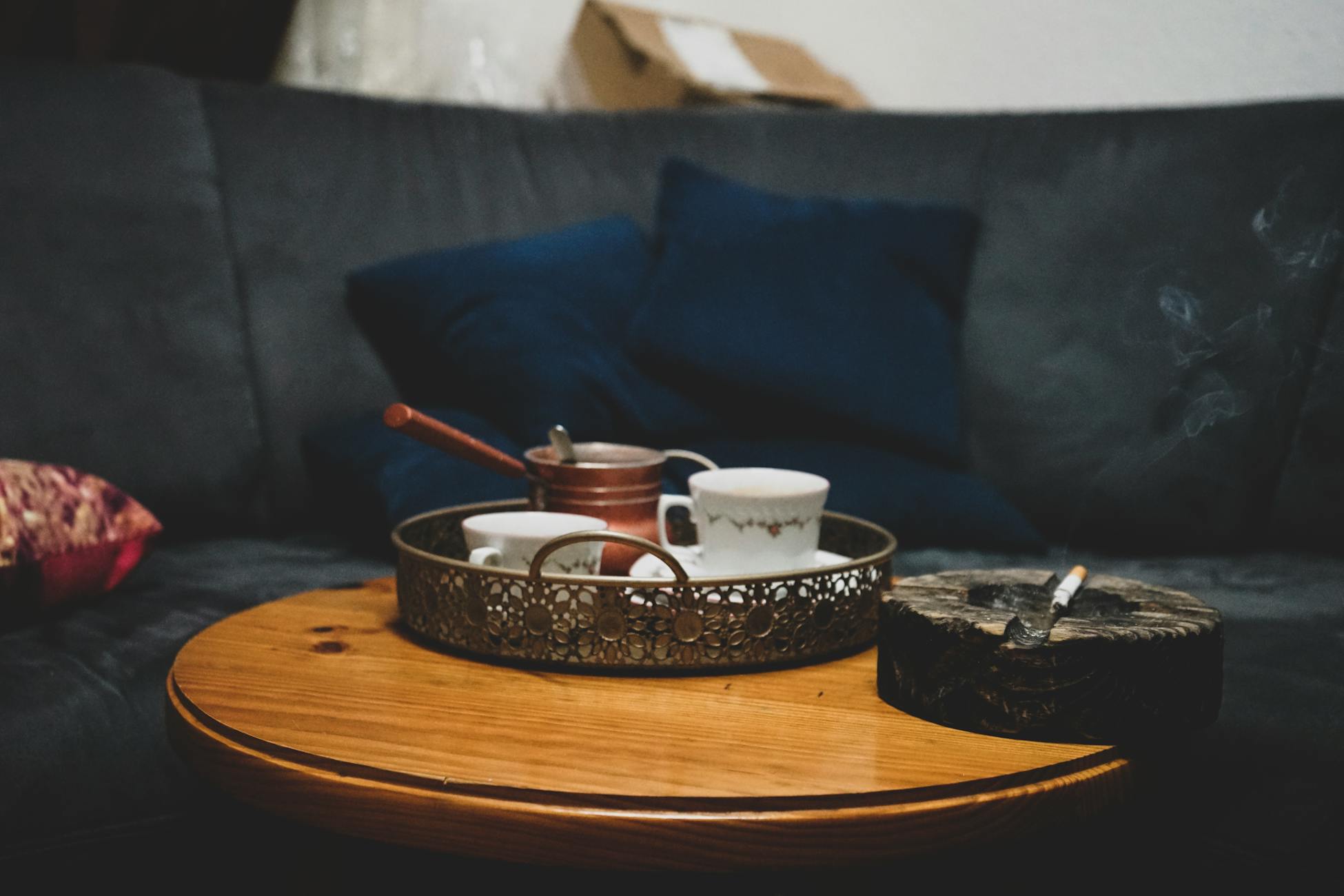 A tranquil setting with a tea set and lit cigarette on a wooden table in a cozy living room.