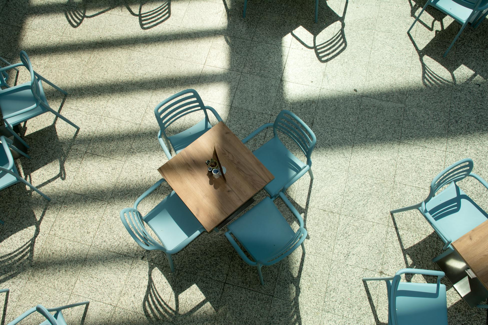 Aerial view of an empty sunlit patio with blue chairs and long shadows.