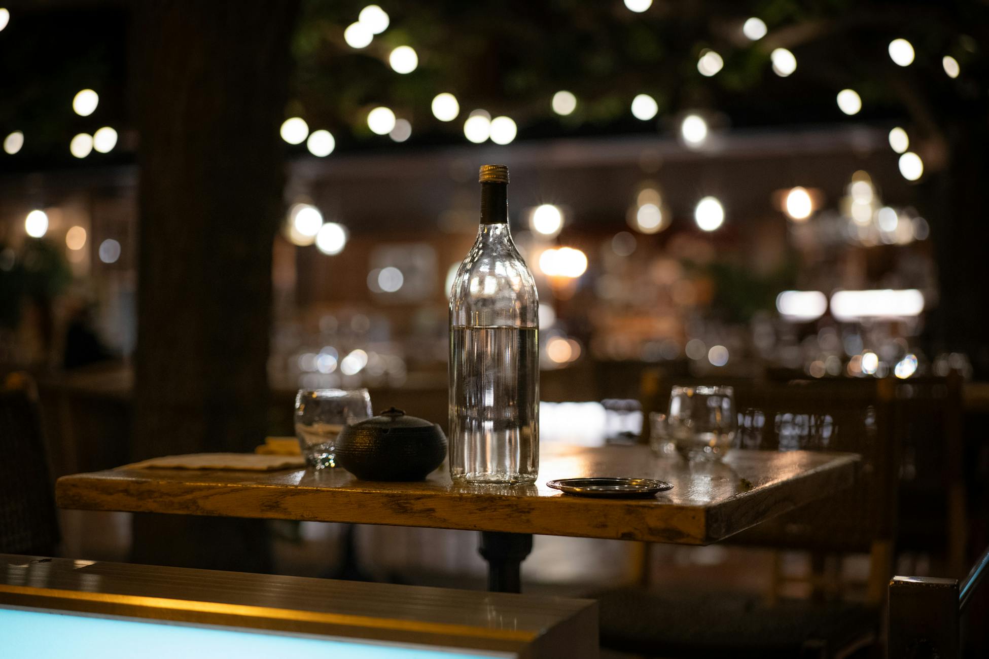 Cozy bar setting with a focus on a glass bottle on a wooden table, perfect for nightlife themes.