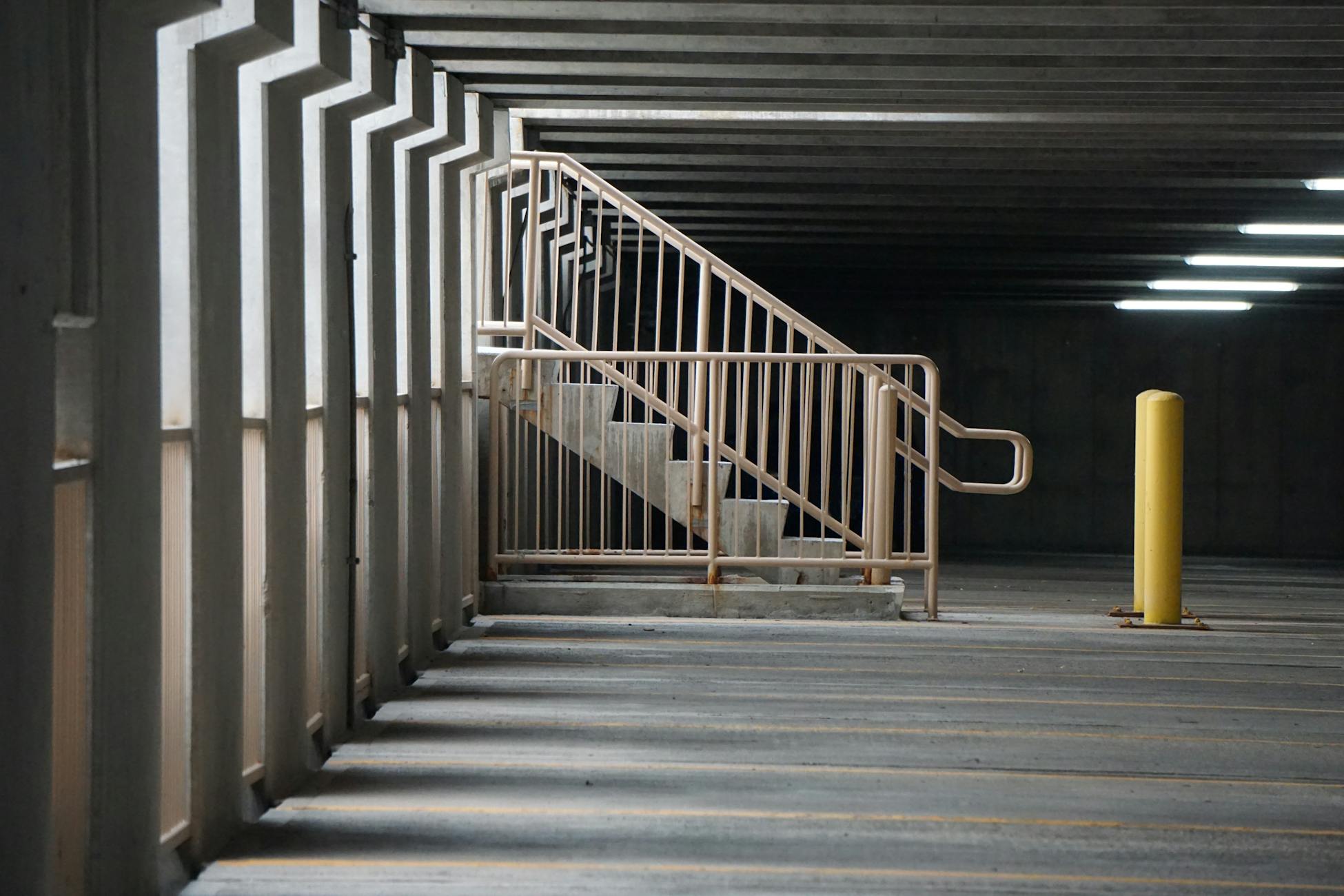 Concrete staircase and railings creating shadows in an empty parking garage.