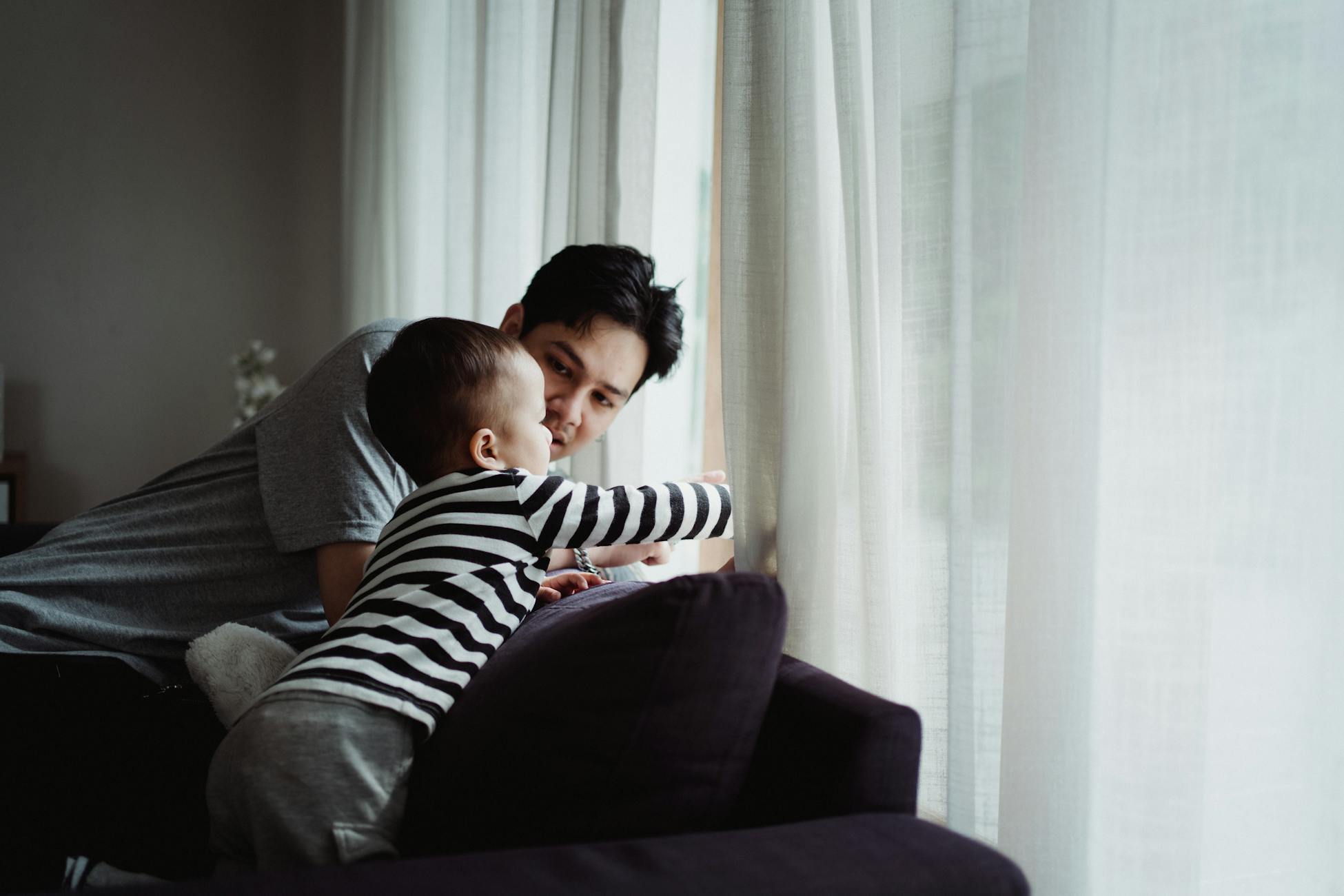 A touching moment between father and son as they look out the window together in a cozy living room.