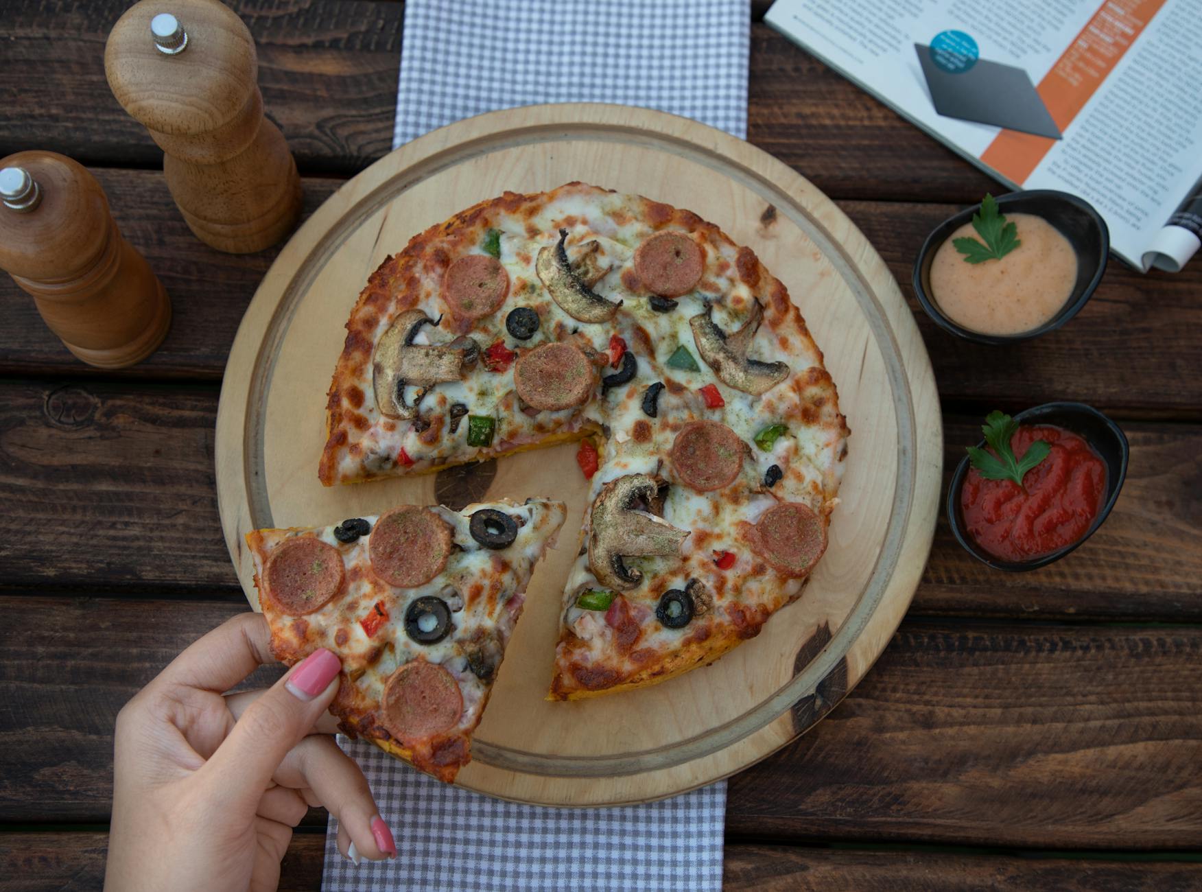 Delicious homemade pizza with olives, mushrooms, and sausage, served with sauces on a wooden table.