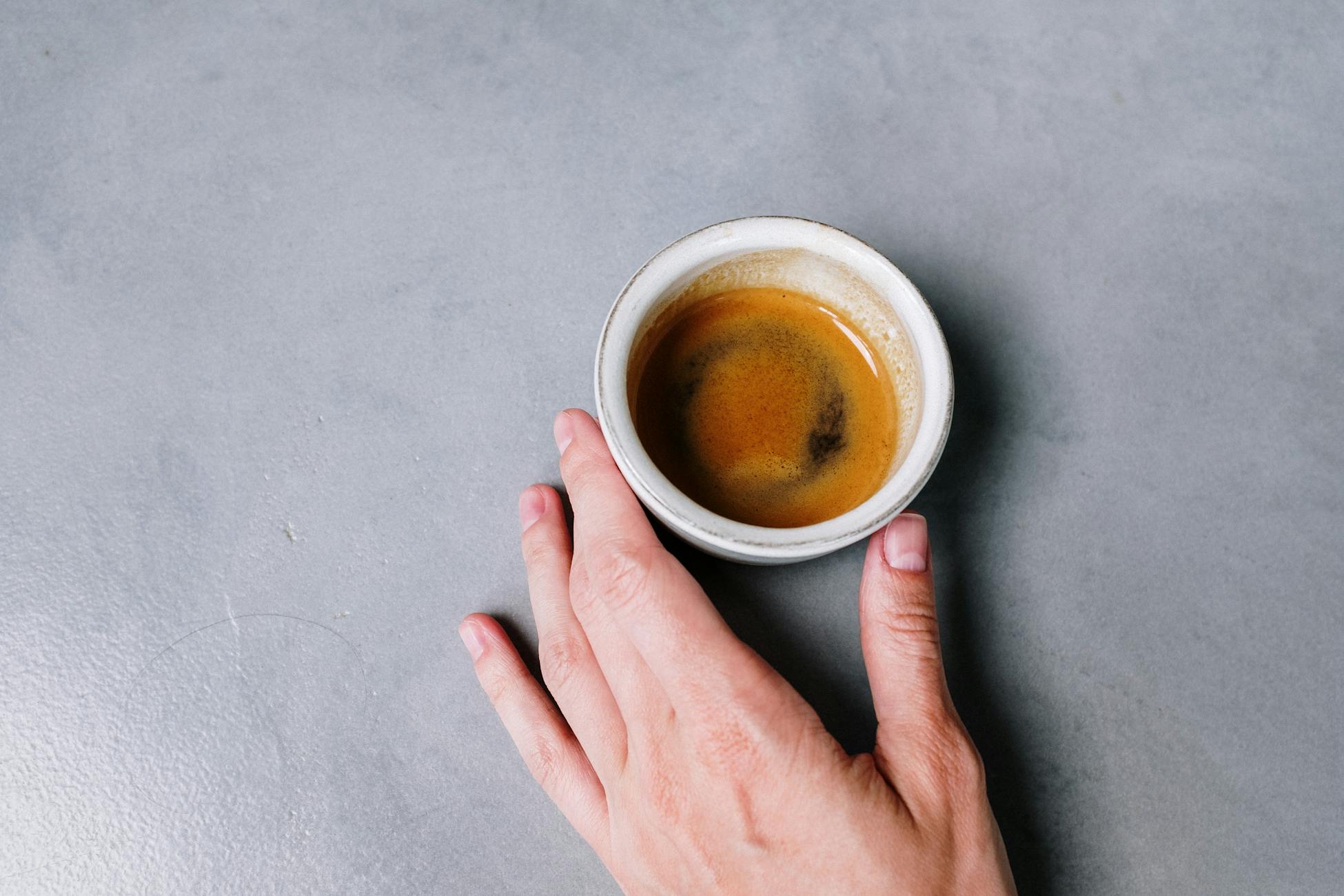 Close-up of a hand holding an espresso cup on a gray concrete surface. Minimalist and modern style.