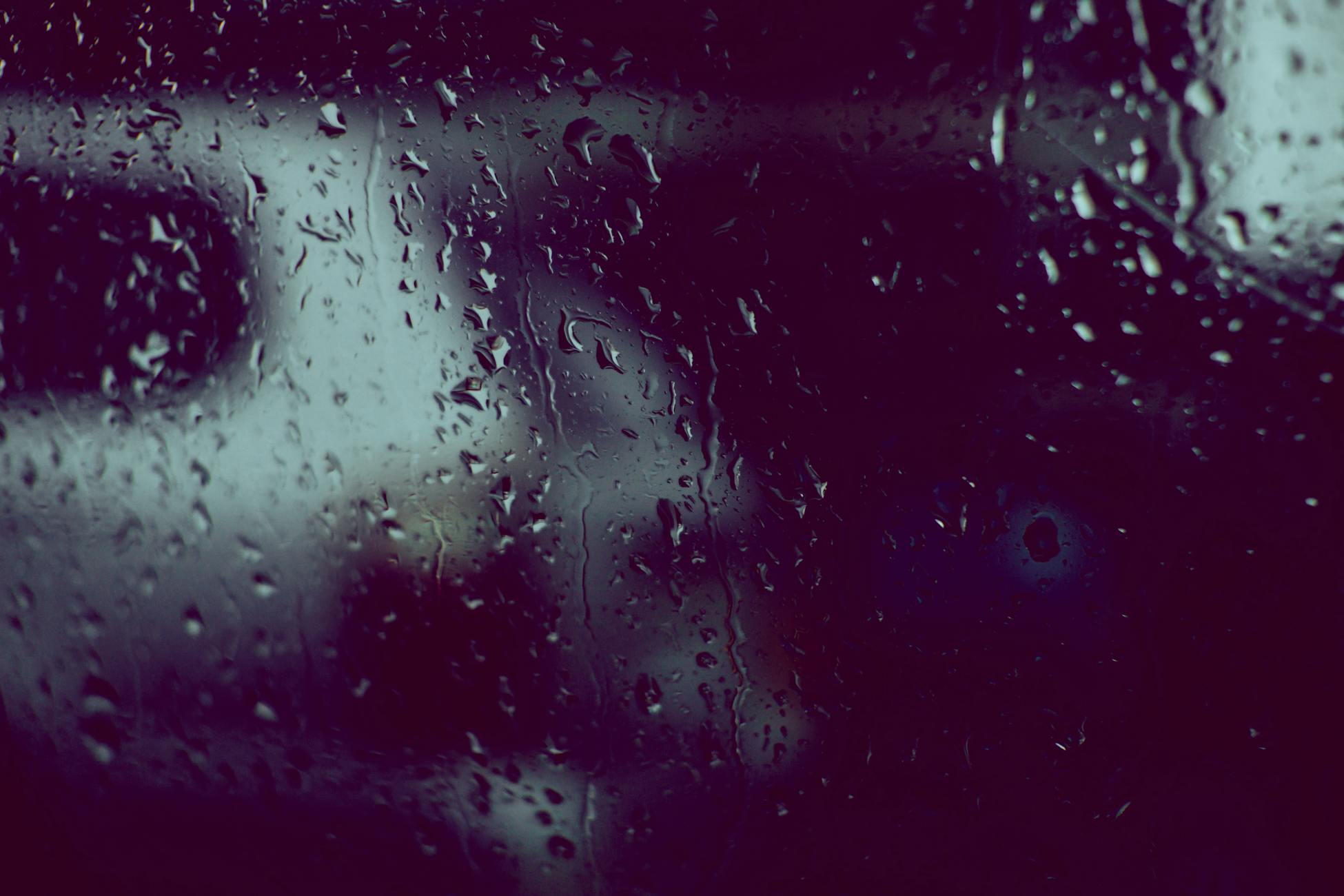 A moody, abstract view of raindrops on a window with a blurred backdrop, capturing a rainy day scene.