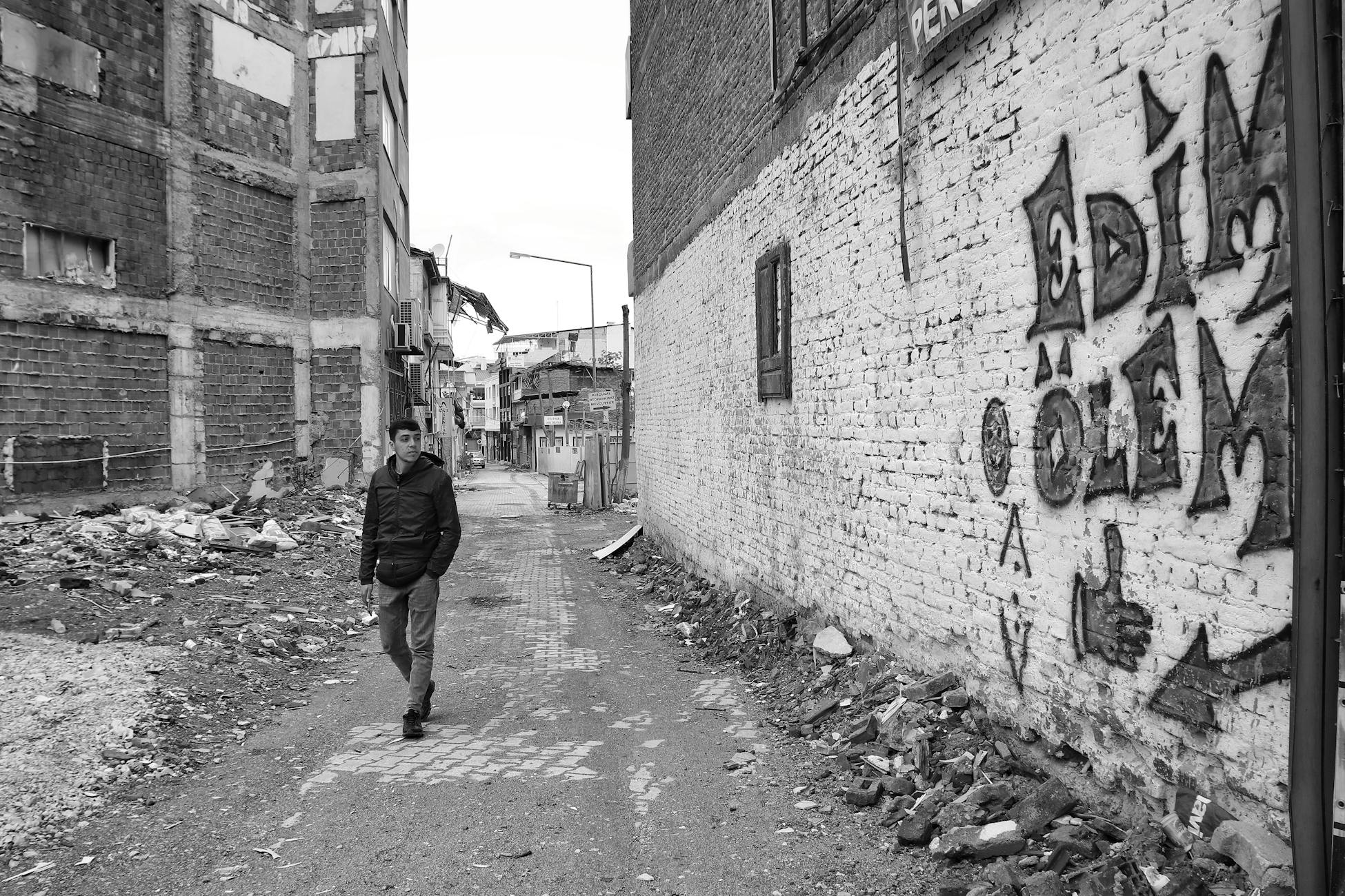 A man walks through a gritty urban alley with graffiti and rubble, showcasing urban decay.