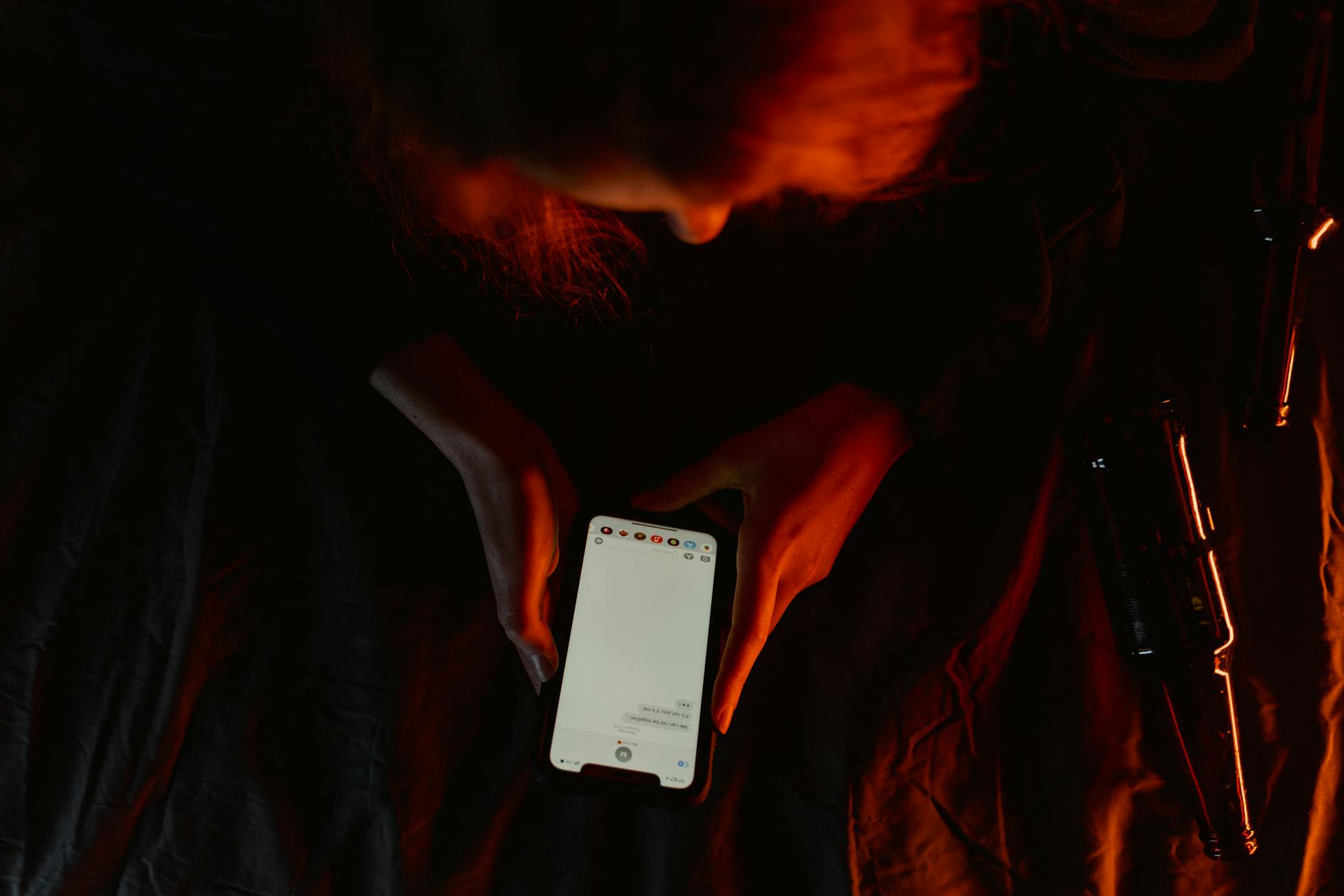 A person using a smartphone in dim, moody lighting with a dark background.