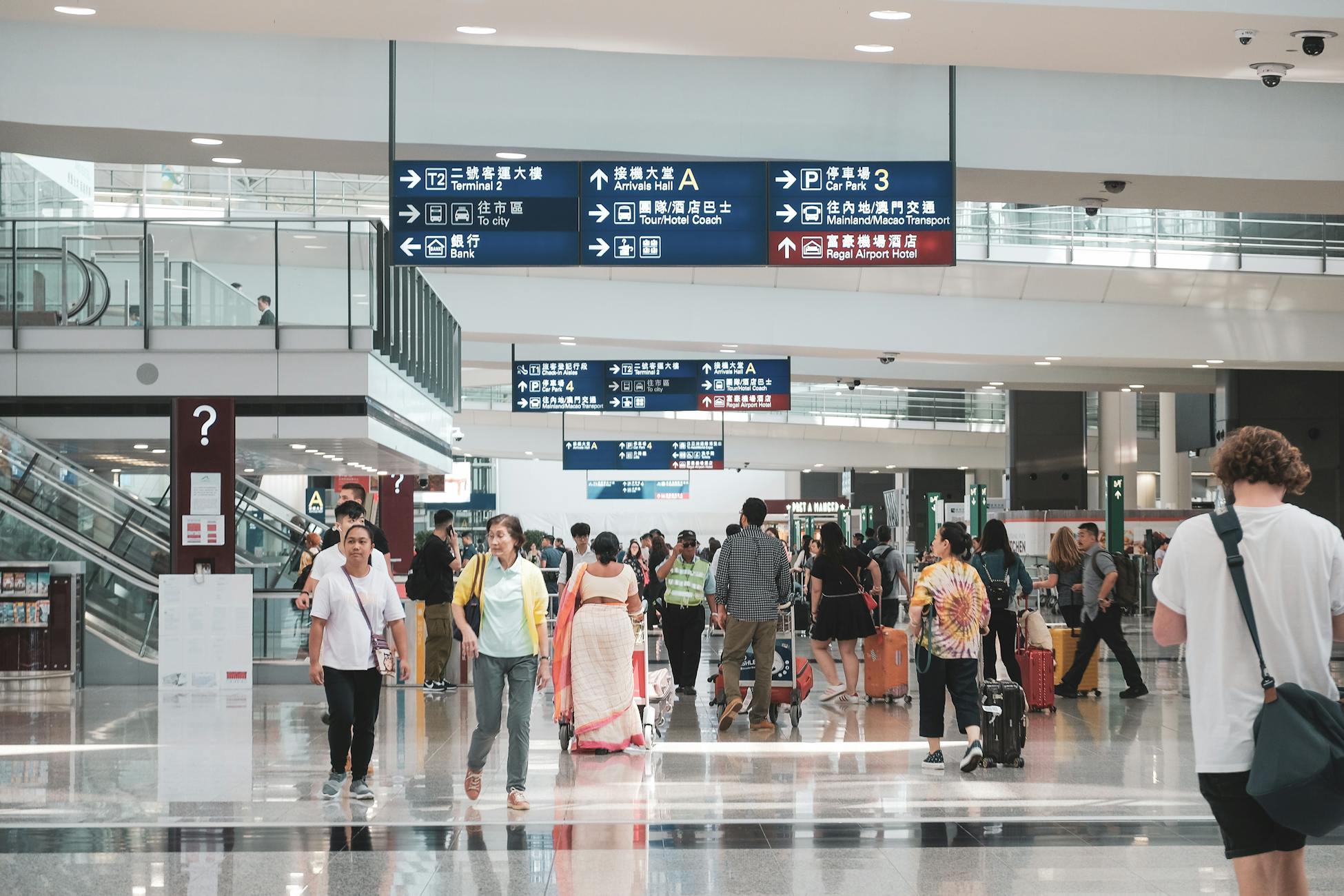 Crowded Hong Kong airport terminal with diverse passengers and informative signage.