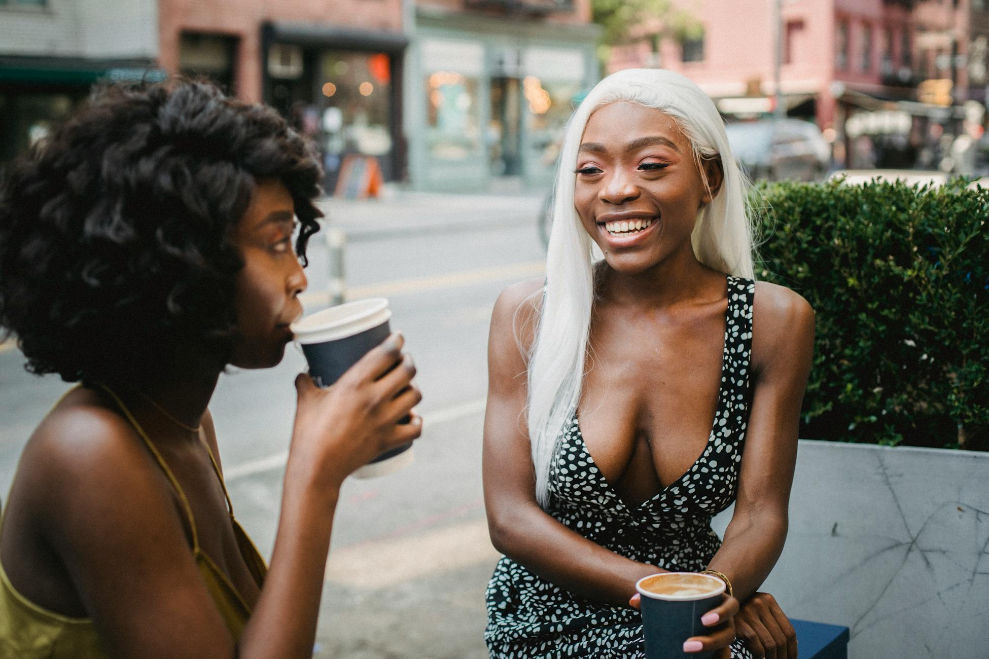 Two women enjoying coffee and conversation at an outdoor cafe on a city street.