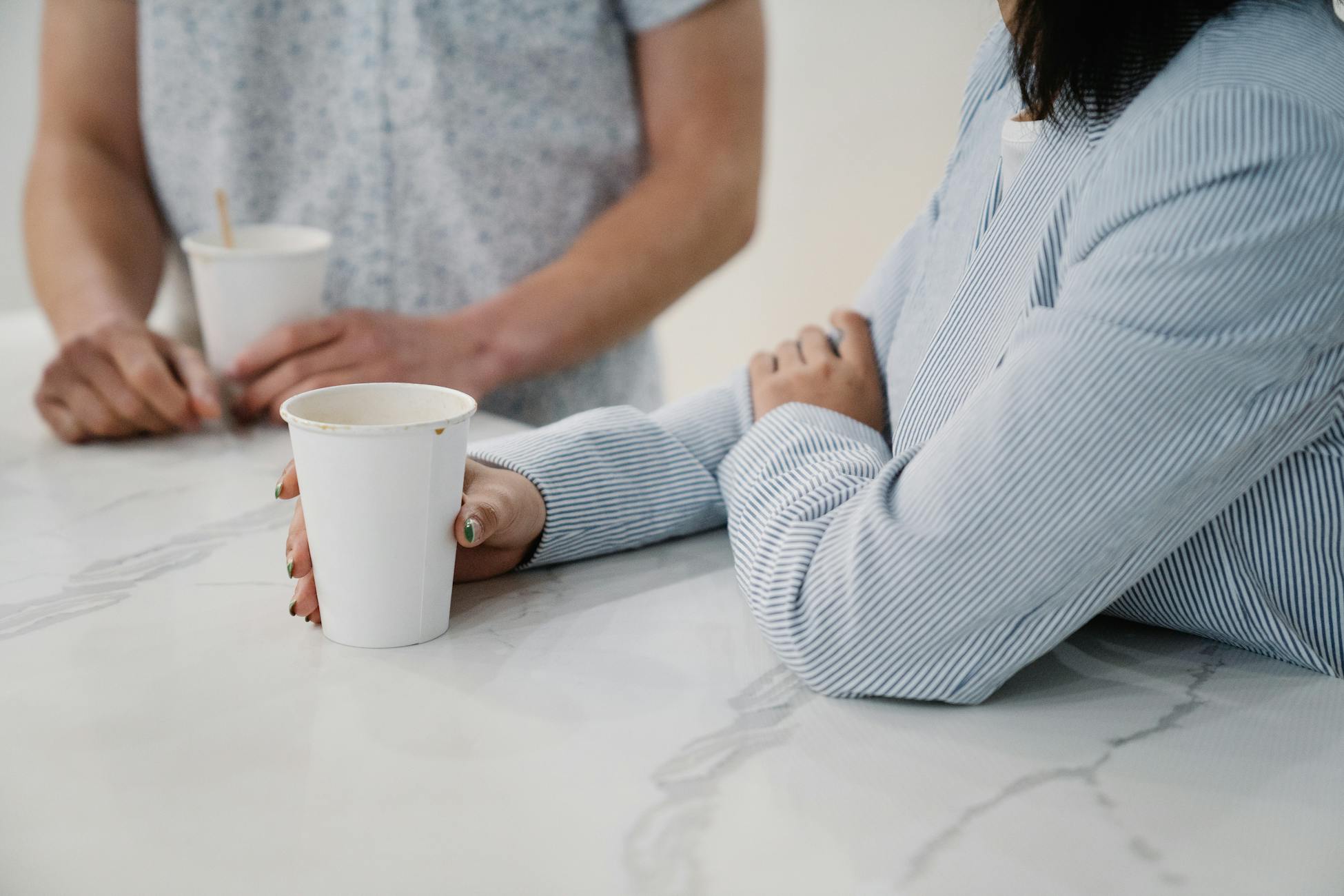 Two people conversing over coffee cups in a modern office setting, promoting a casual work atmosphere.