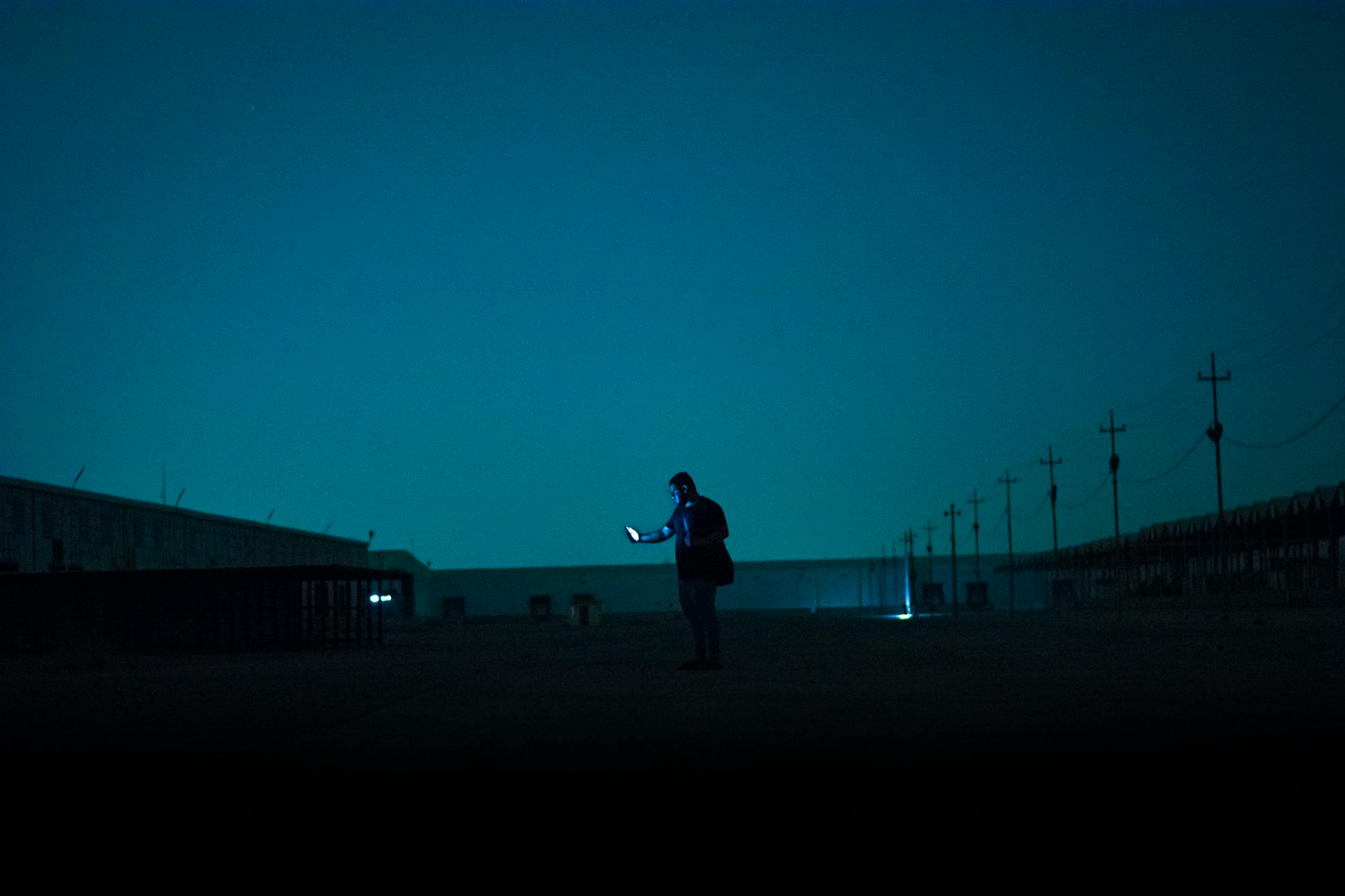 Silhouette of a solitary person at night illuminated by phone light, creating a moody atmosphere.