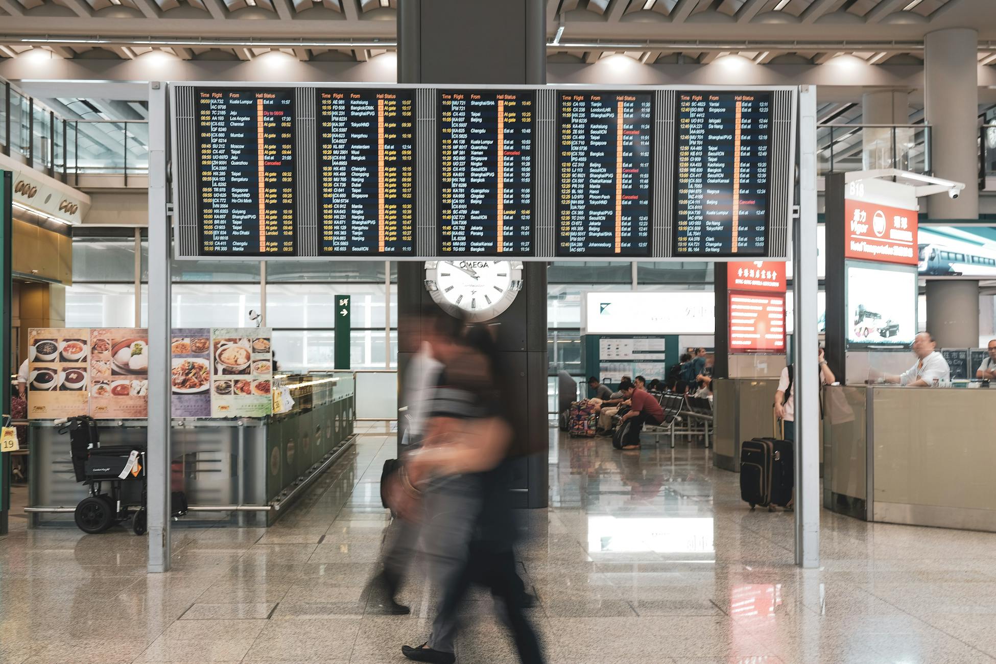 Blurred motion of travelers in a modern airport terminal with departure screens and a prominent clock.