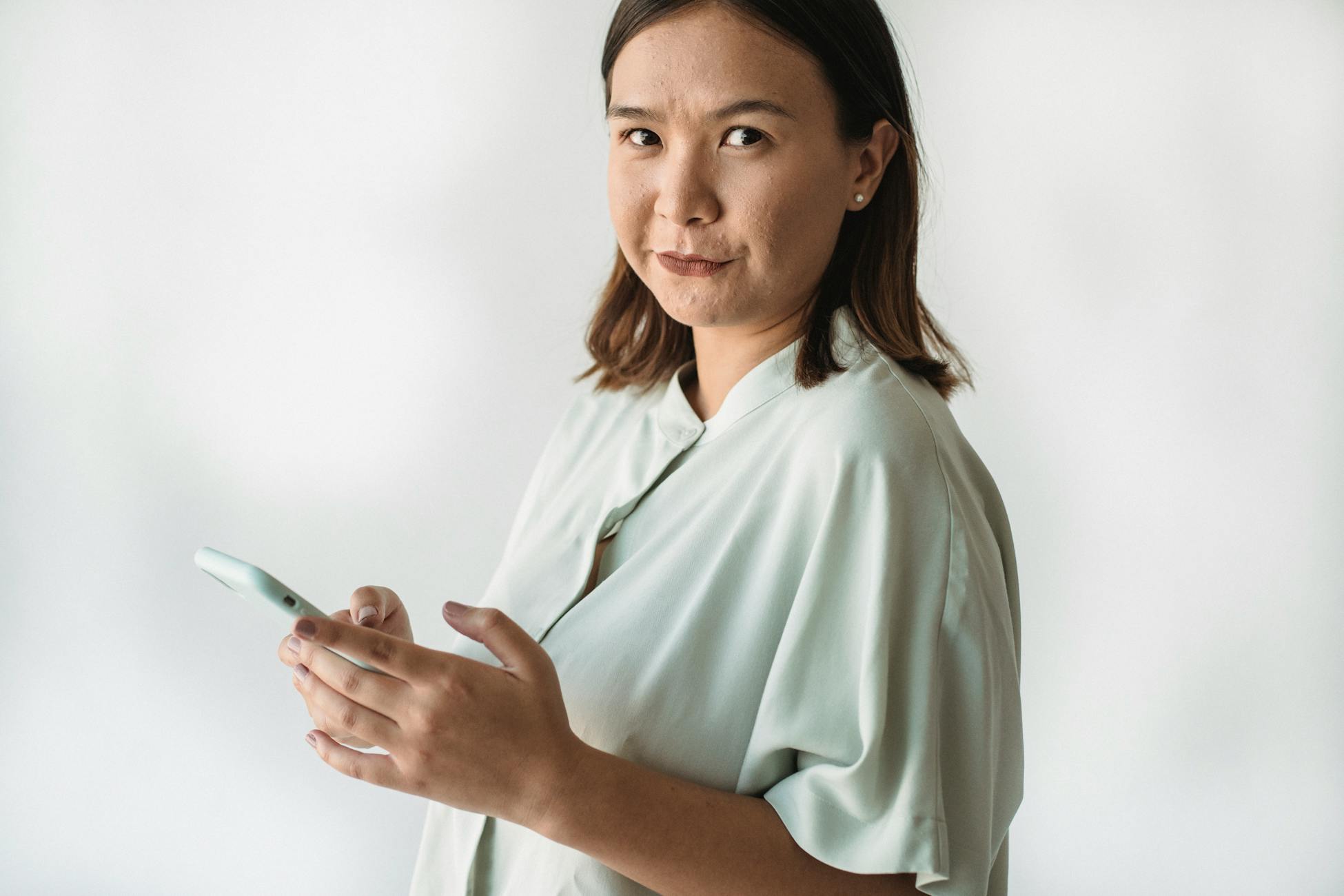 Portrait of an adult Asian woman in business attire using a smartphone indoors.