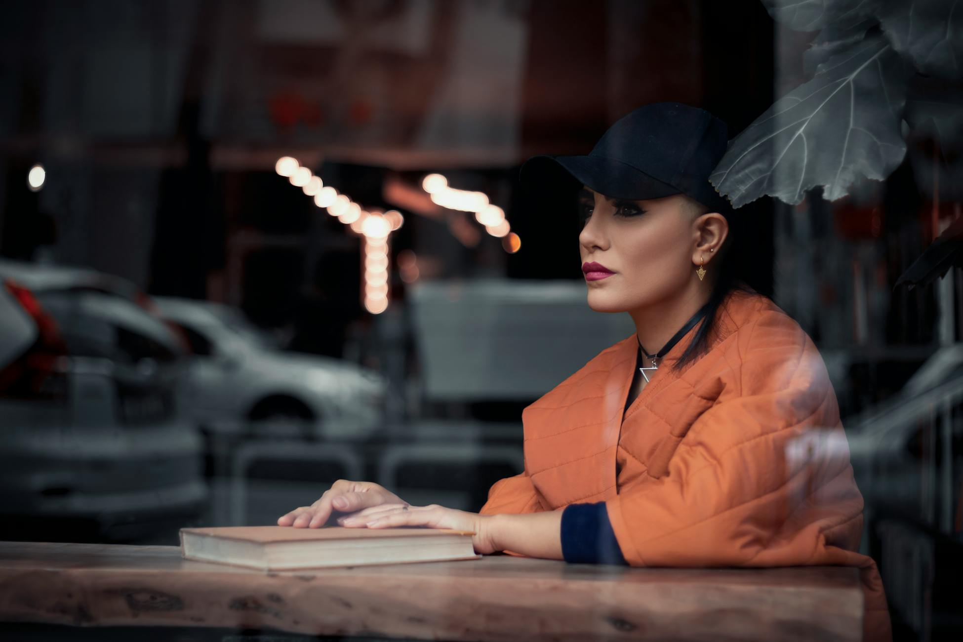 Fashionable woman wearing a cap sits thoughtfully by a glass window in Tehran.