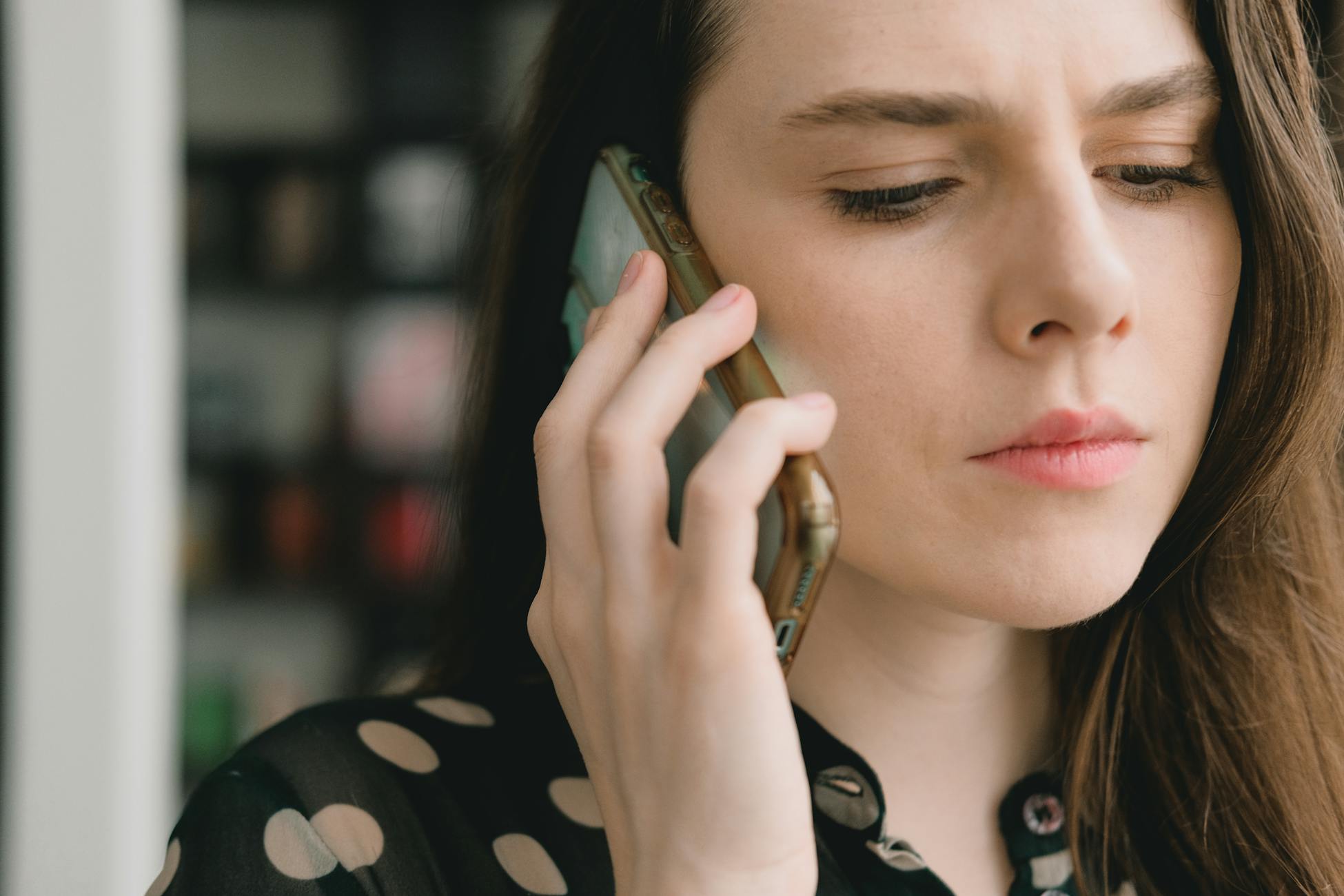 Close-up of a woman engaged in a phone conversation indoors, depicting a thoughtful expression.