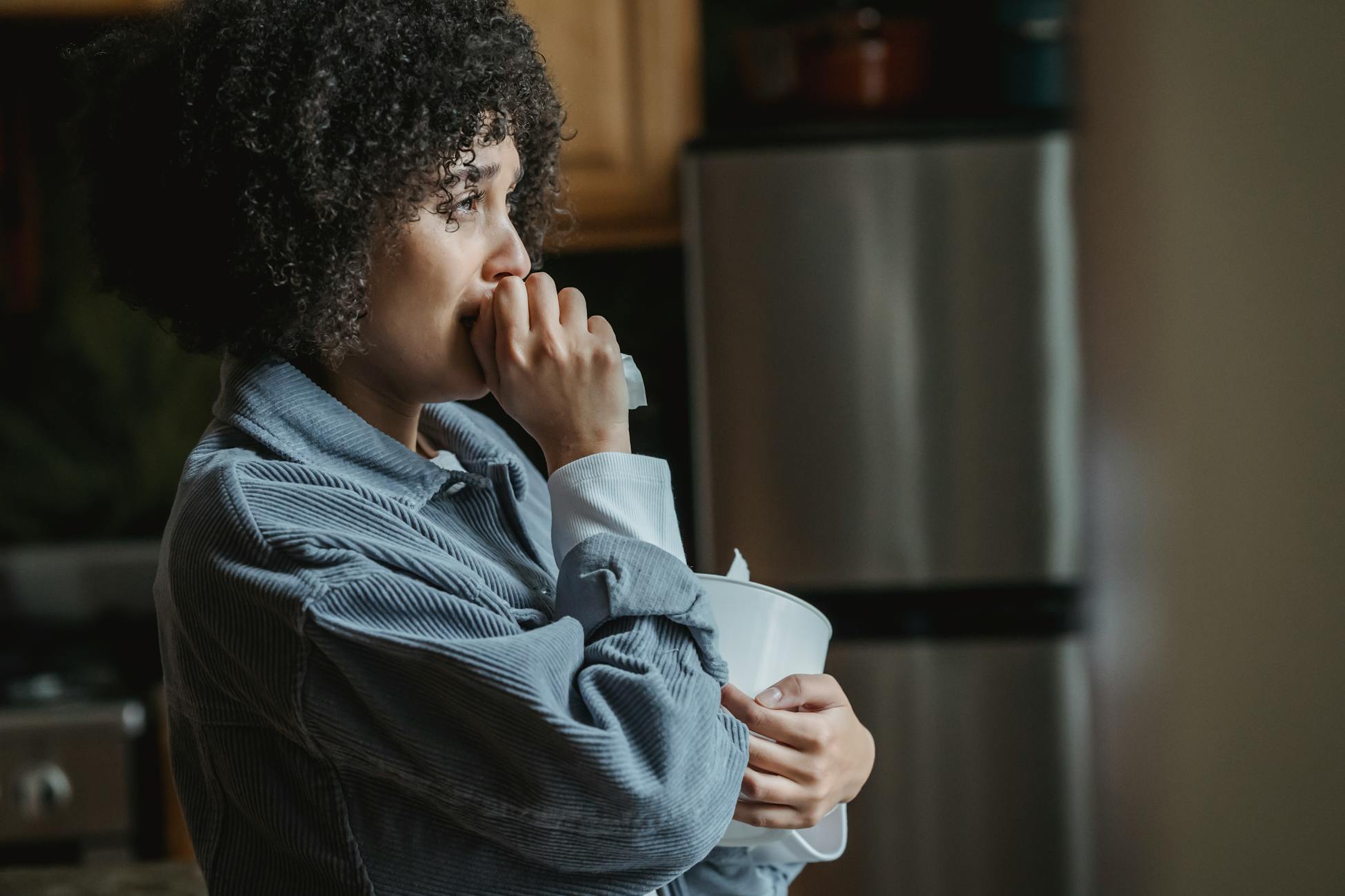 Side view of crying African American female with tissue sorrowing from unhappiness and grief in kitchen