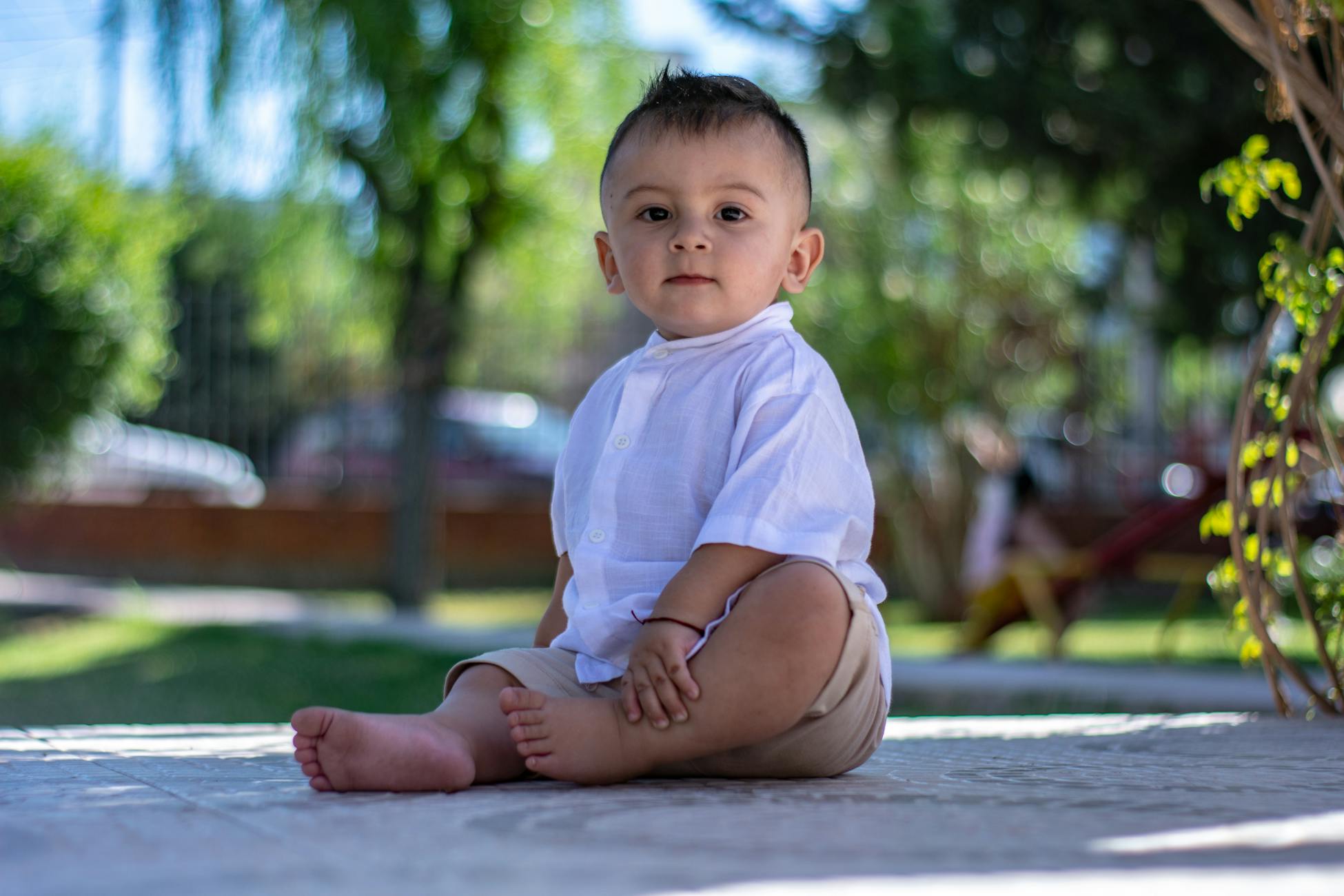 Charming baby sitting outdoors in summer fashion attire, bright and engaging expression.