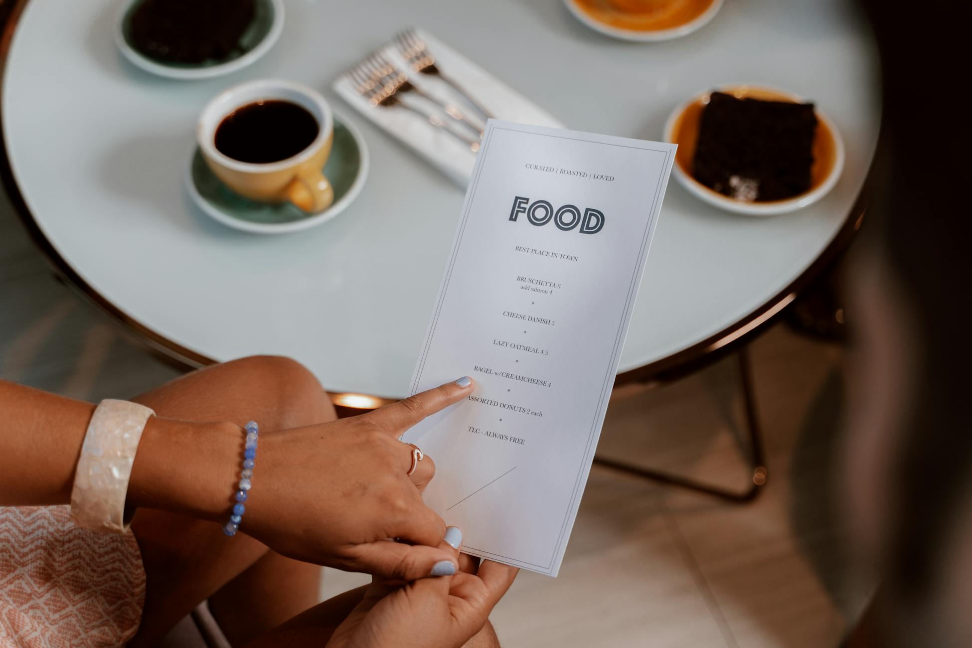 Hands holding a menu, selecting options at a cozy cafe with coffee and dessert on the table.