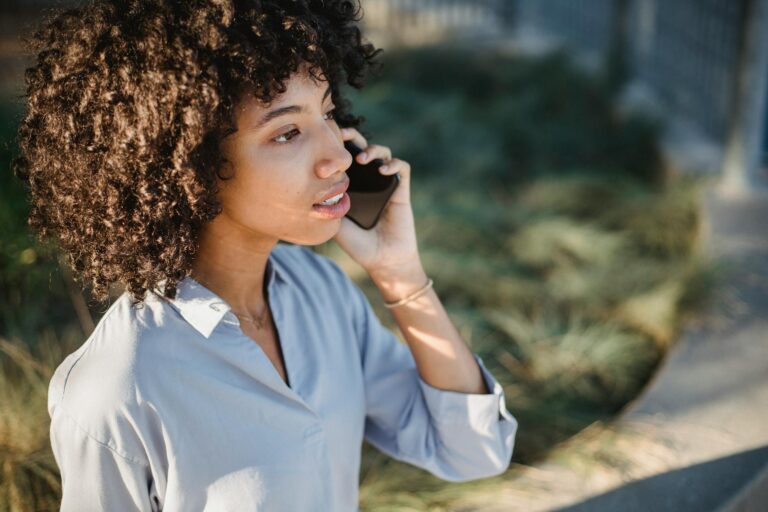 Crop African American female in casual clothes standing on street and talking on smartphone while looking away
