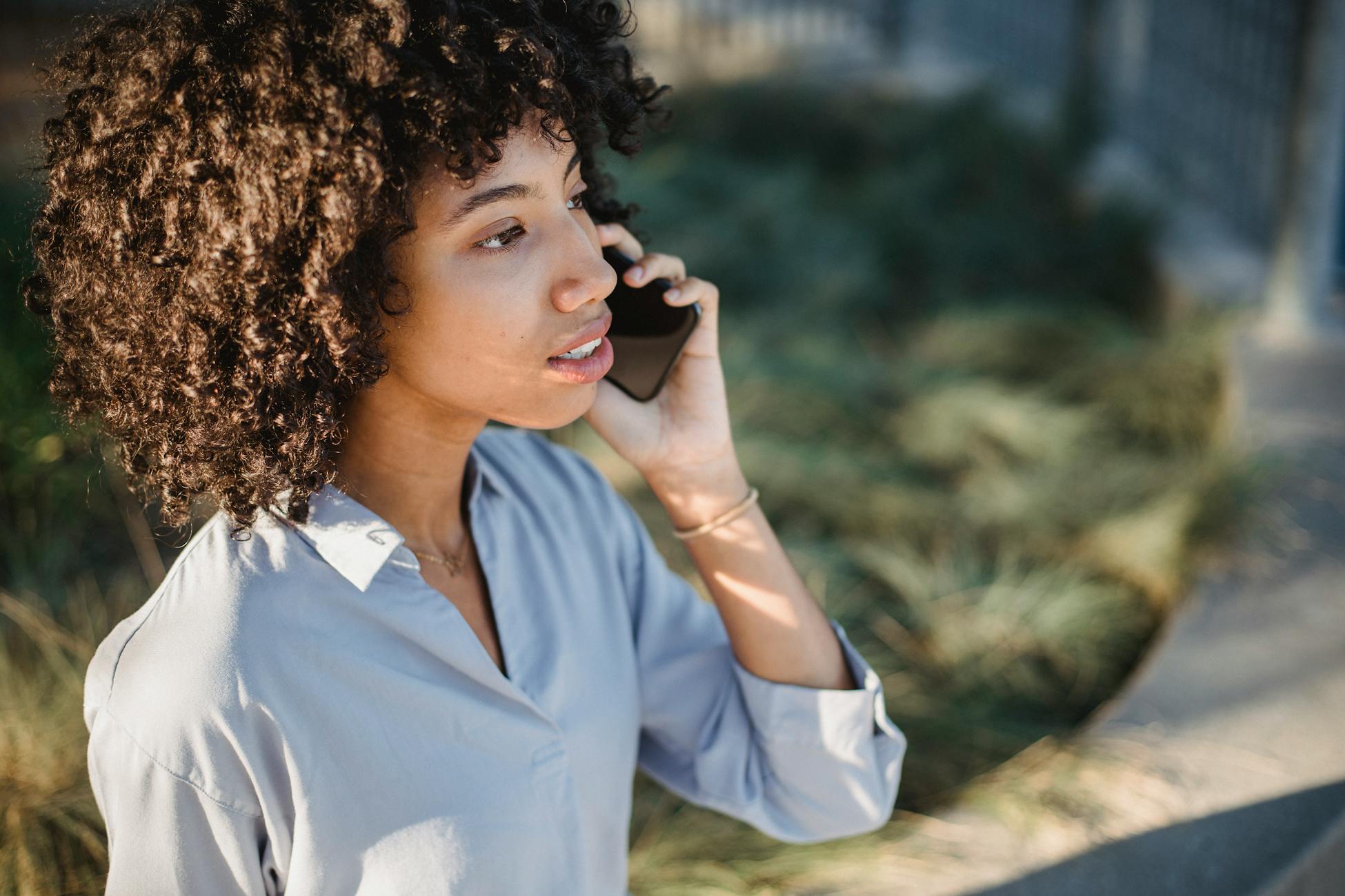 Crop African American female in casual clothes standing on street and talking on smartphone while looking away