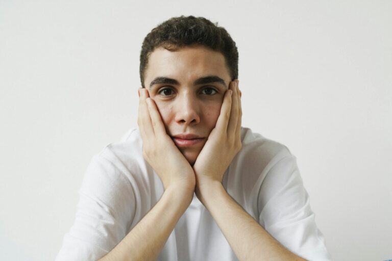 Portrait of a young man with hands on cheeks, wearing a white t-shirt.