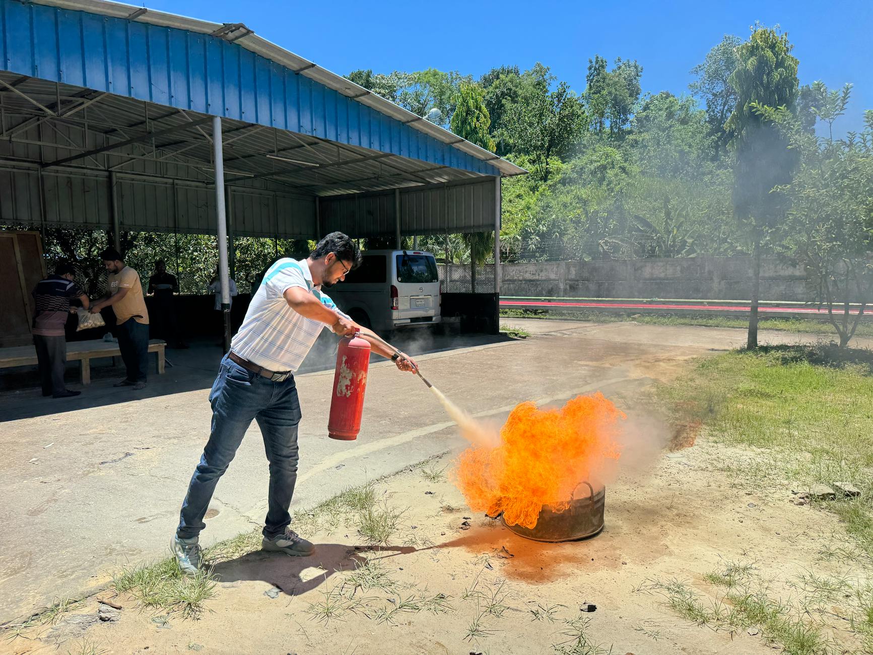 A man uses a fire extinguisher to put out a controlled fire during an outdoor safety training session.