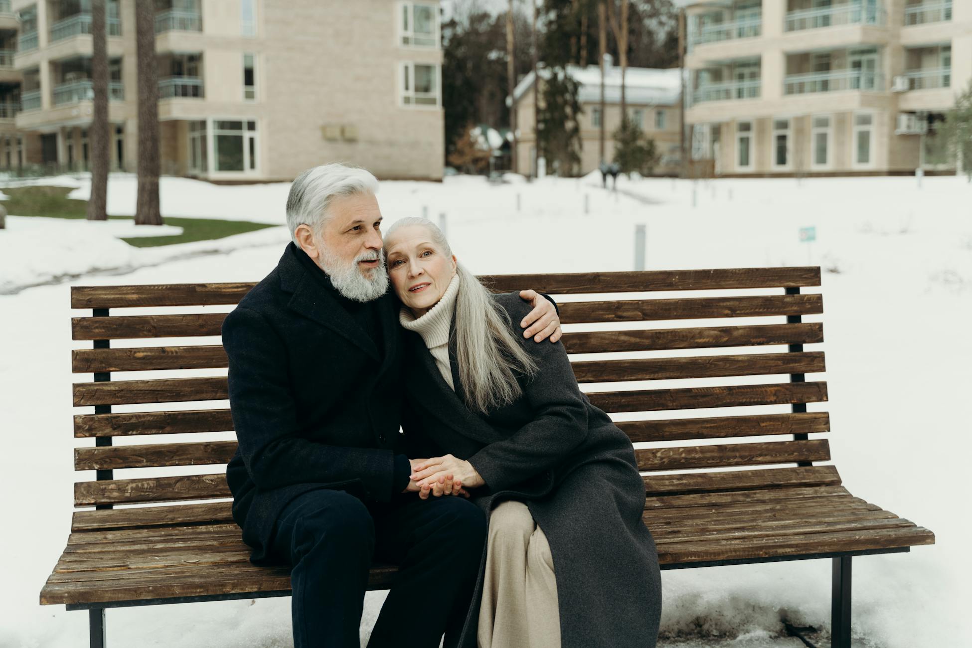 Elderly couple embracing on a bench in a snowy outdoor setting, showcasing love and togetherness.