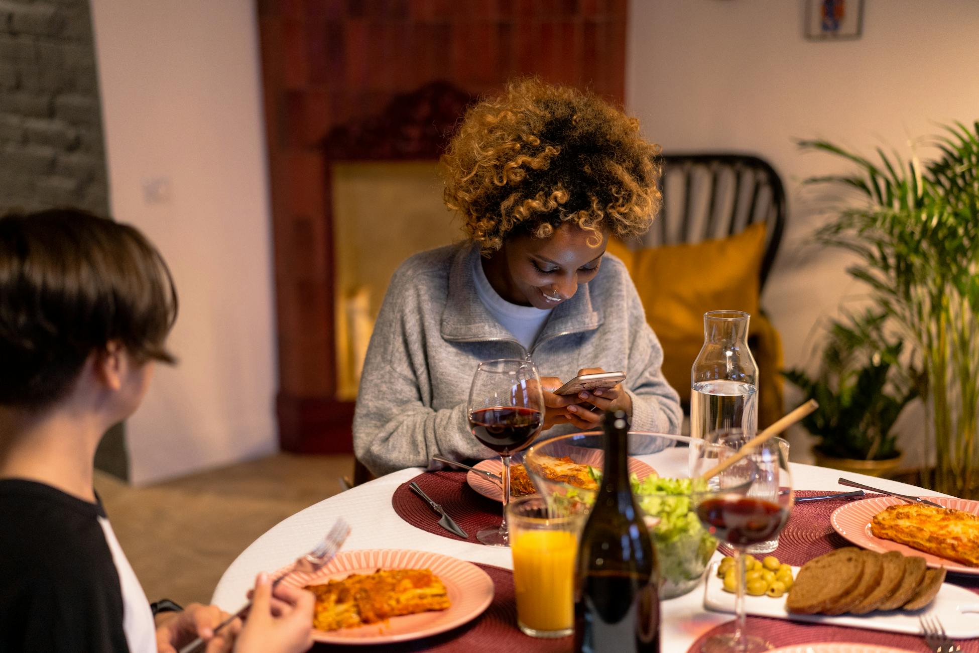 Two friends enjoy a cozy dinner indoors, sharing laughter and conversation over pasta and wine.