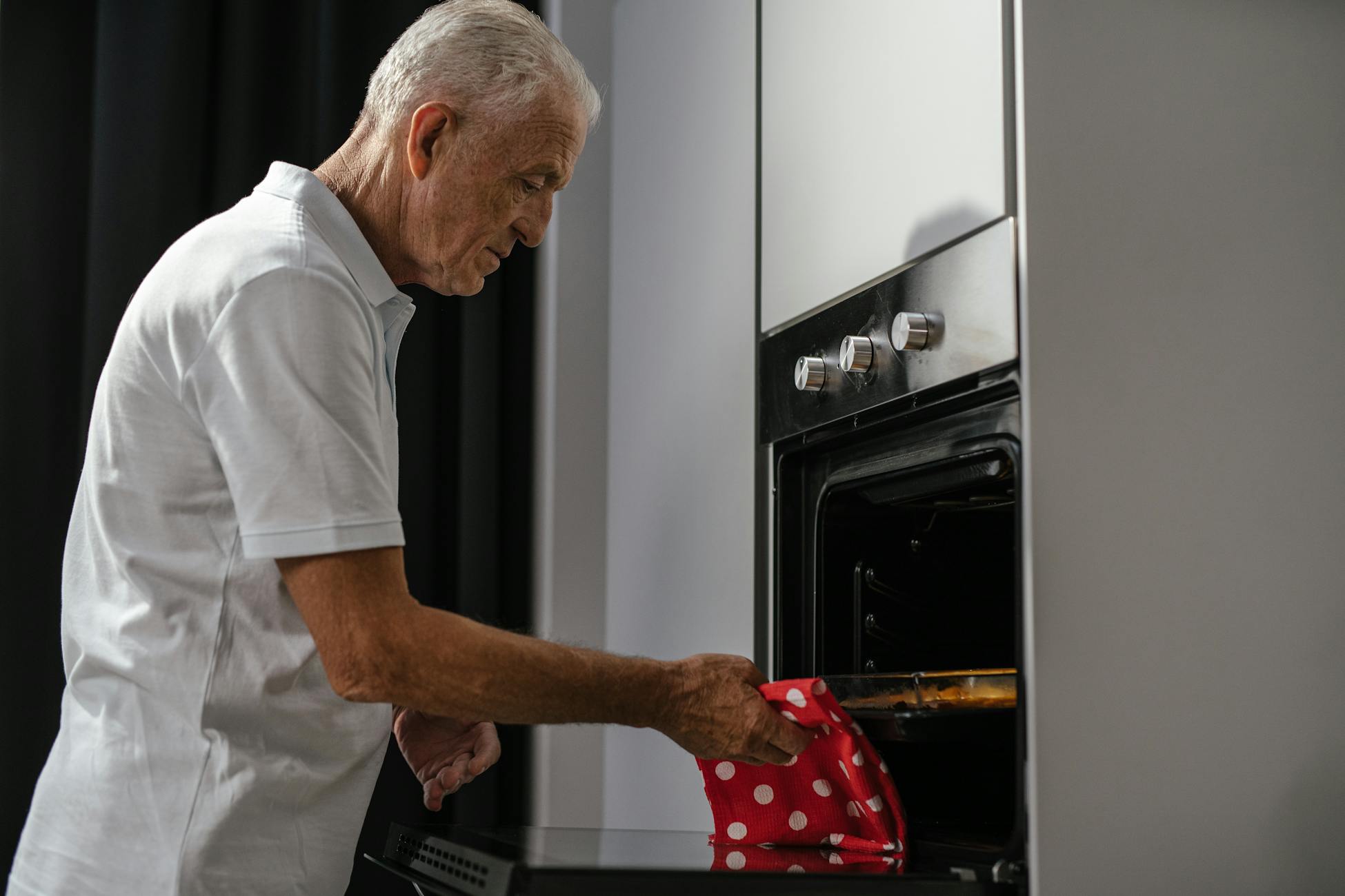 A senior man in a white shirt using an oven in a modern kitchen setting.