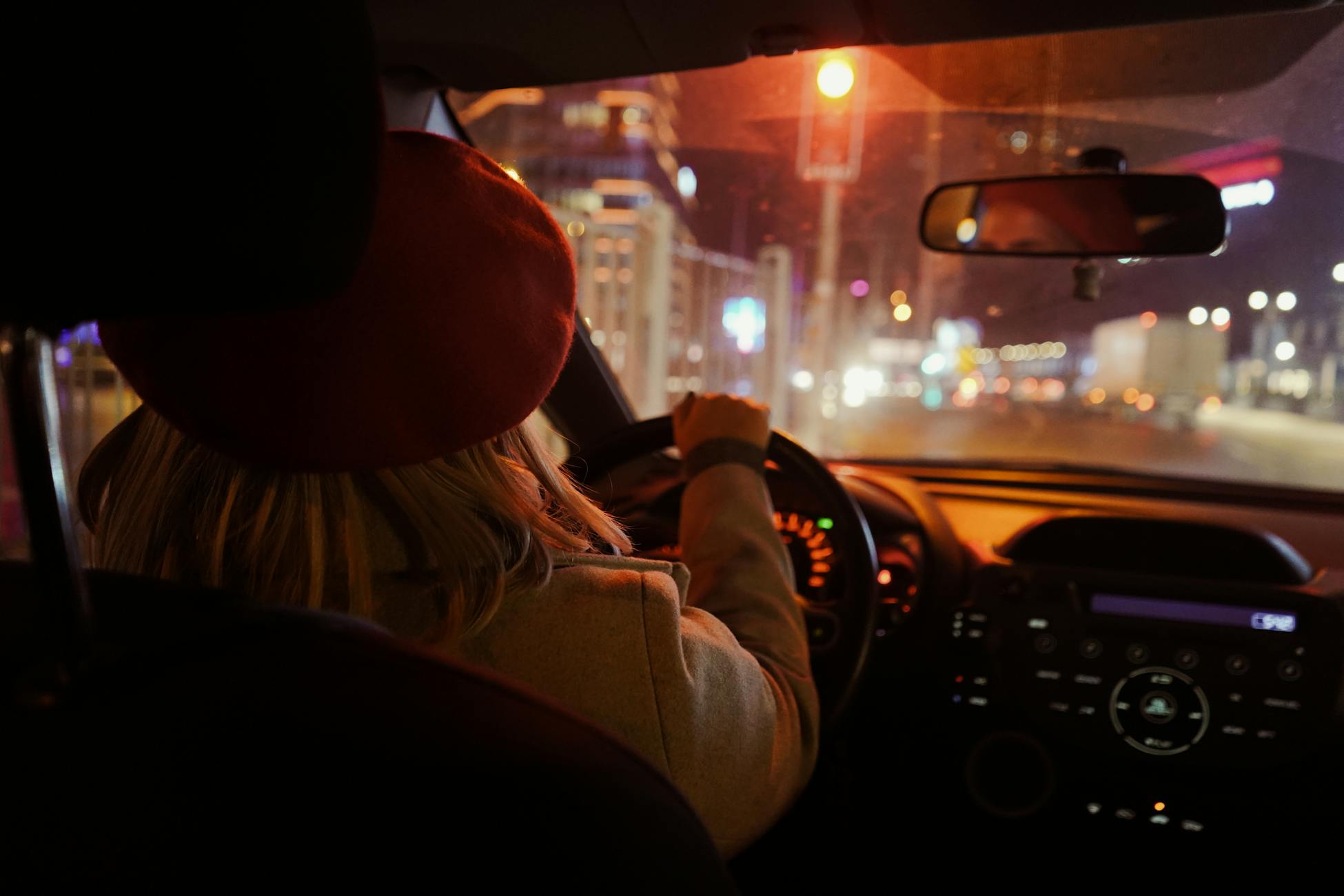 Rear view of a woman driving through Istanbul at night, city lights illuminating the journey.