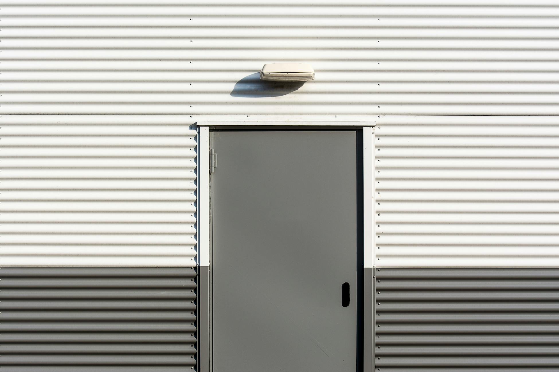 Minimalist image of a corrugated metal wall with a centered door, showcasing industrial architecture.