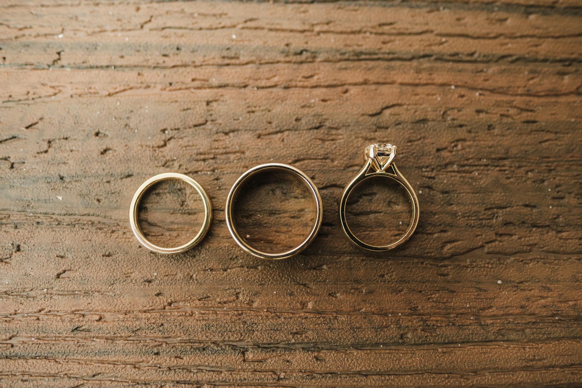 Close-up of gold and diamond rings displayed on a rustic wooden surface.