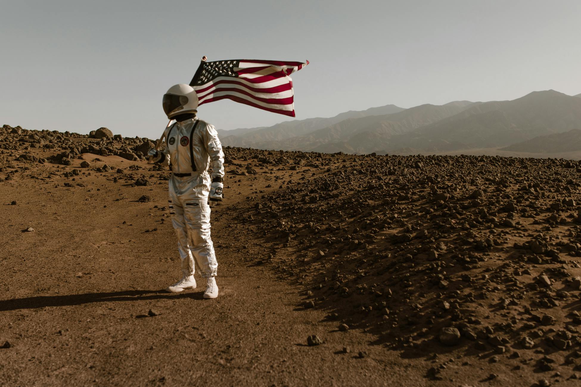 Astronaut standing on barren landscape holding American flag. Conceptual space exploration image.