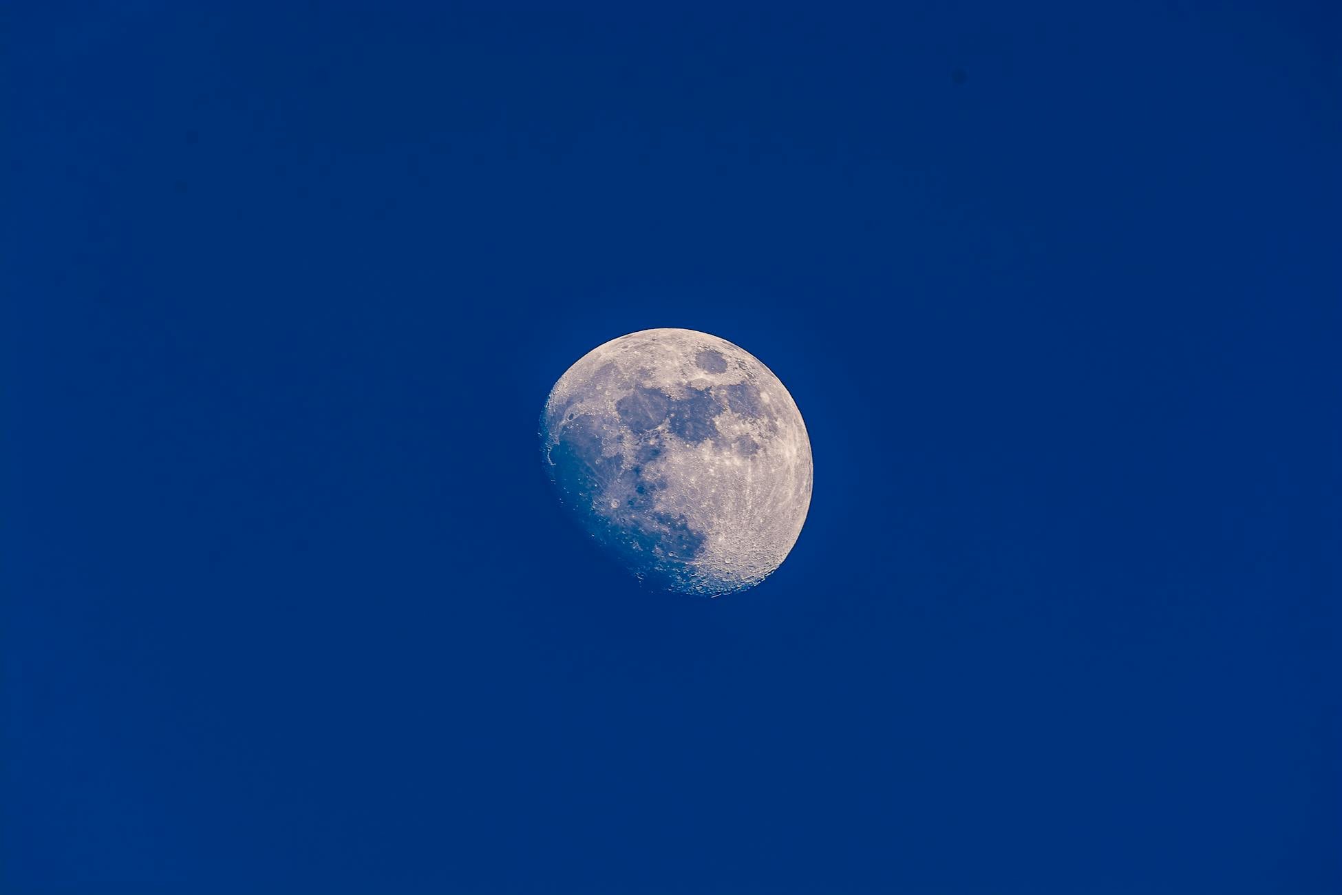 A clear view of the waxing gibbous moon set against a vibrant blue sky, showcasing lunar details.