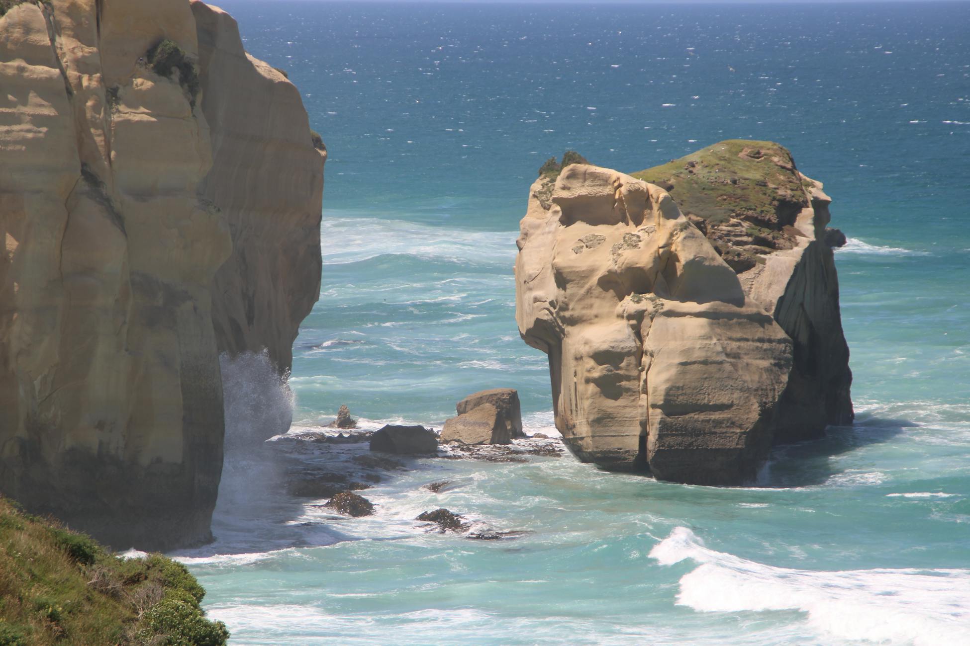 Stunning rocky coastal formations with waves crashing against them on a sunny day.