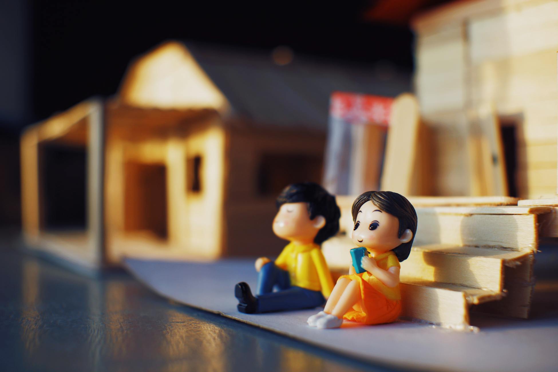 Cute figurines of boy and girl placed on table with toy decorative houses with stair in light room at home