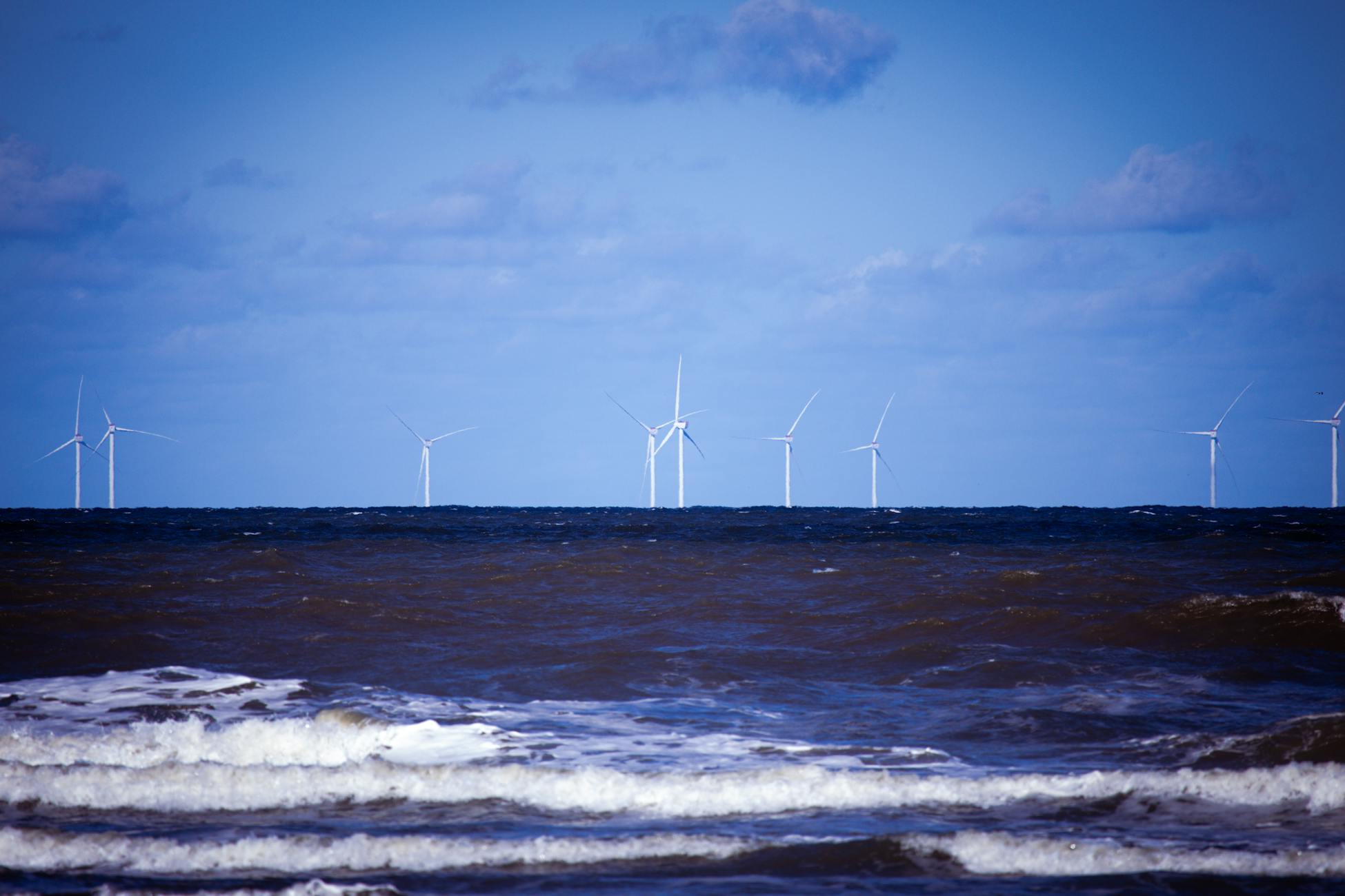 Offshore wind turbines generating sustainable energy over a calm ocean under a clear blue sky.
