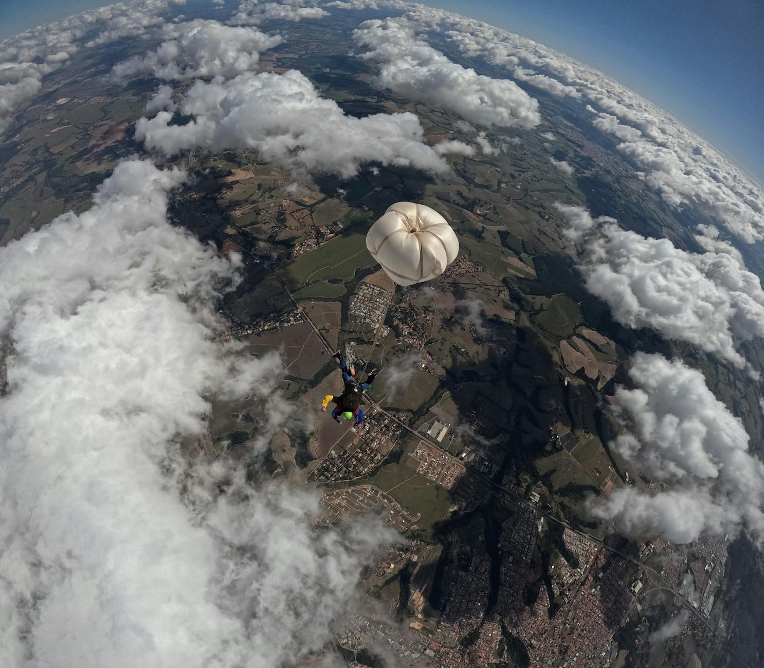 Skydiver descending with parachute over a vast landscape, surrounded by clouds.