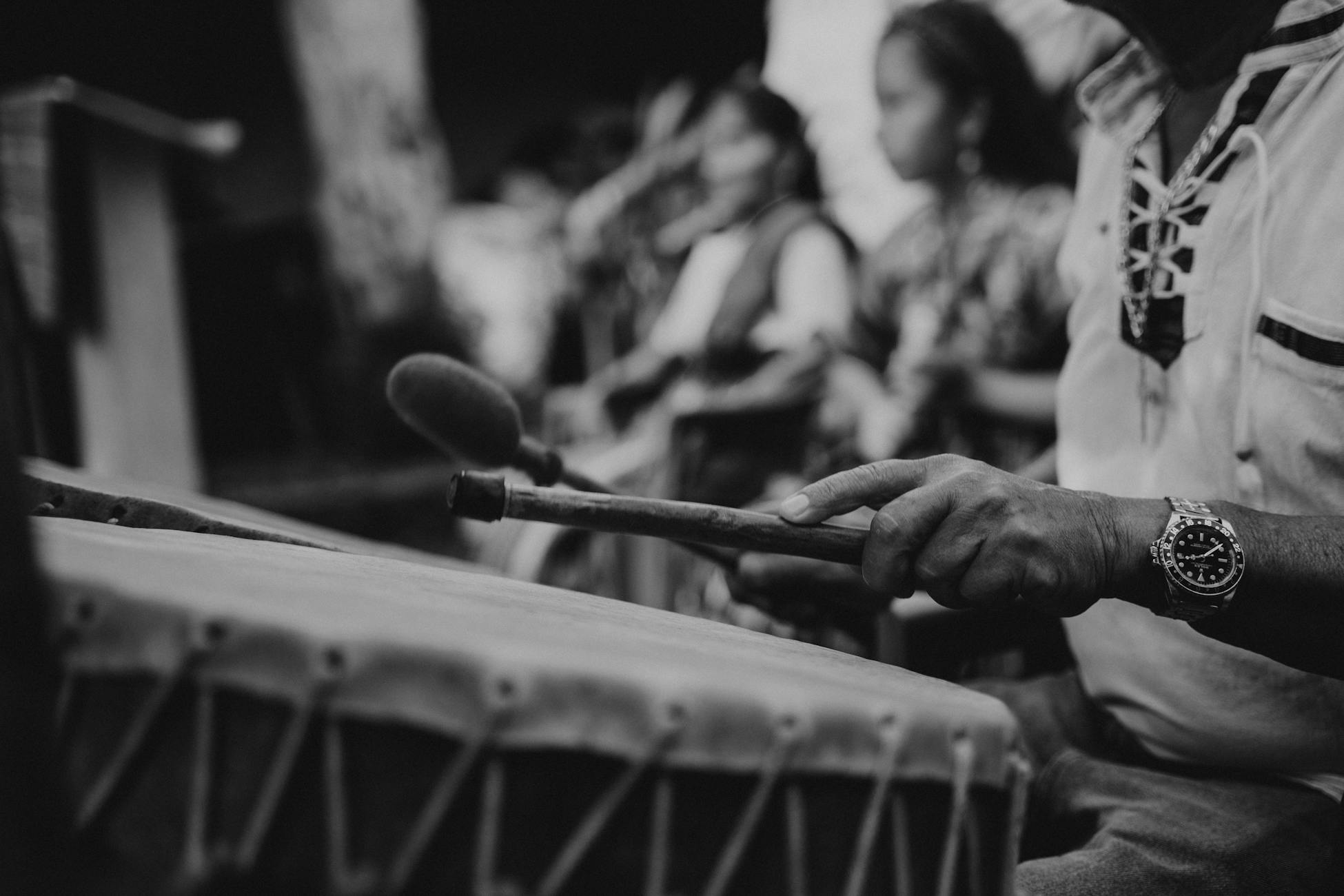 Striking black and white image of a drummer performing at an outdoor event with blurred background.