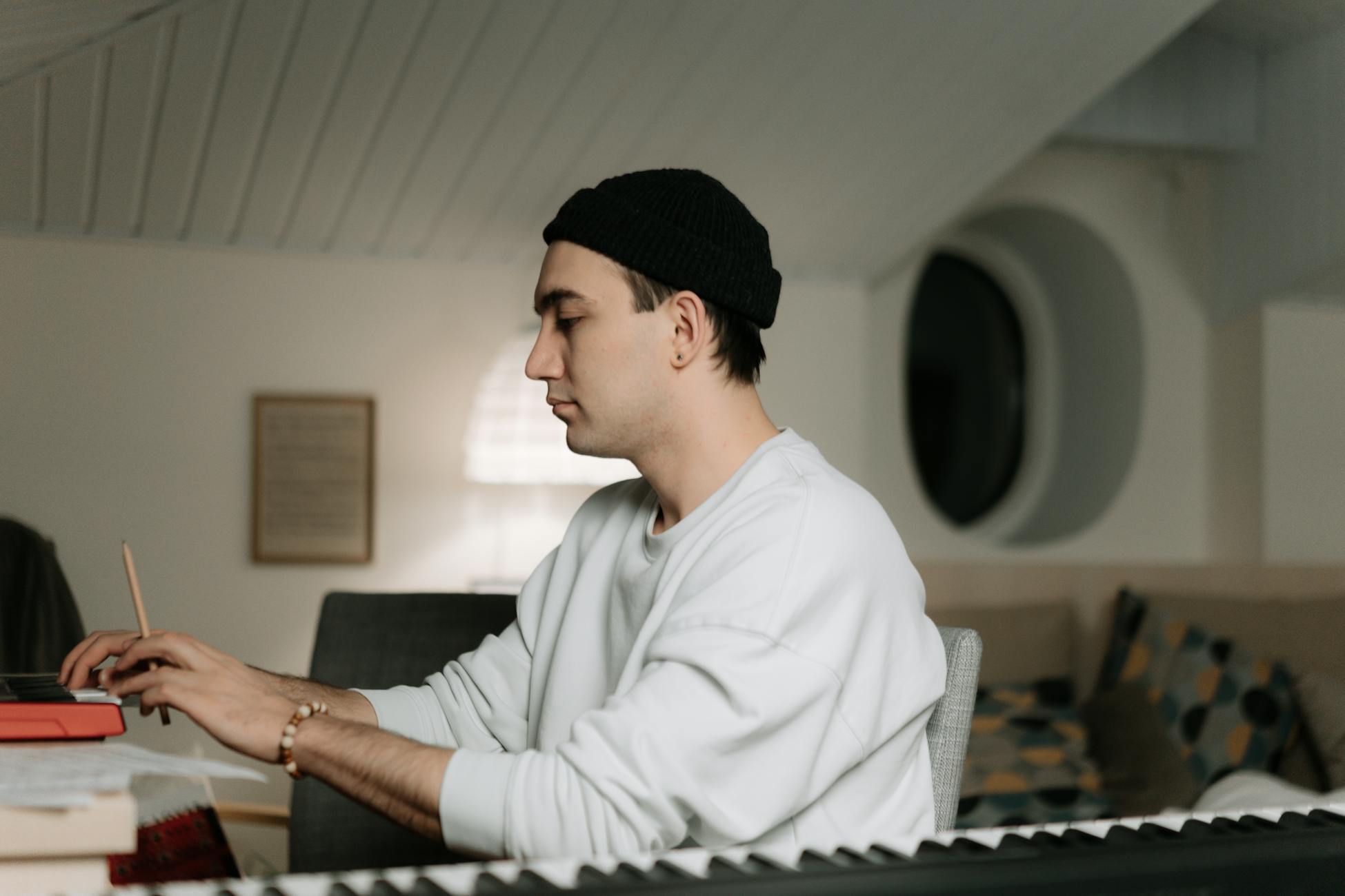 A young musician composing music indoors, focused on playing the keyboard in a cozy room.