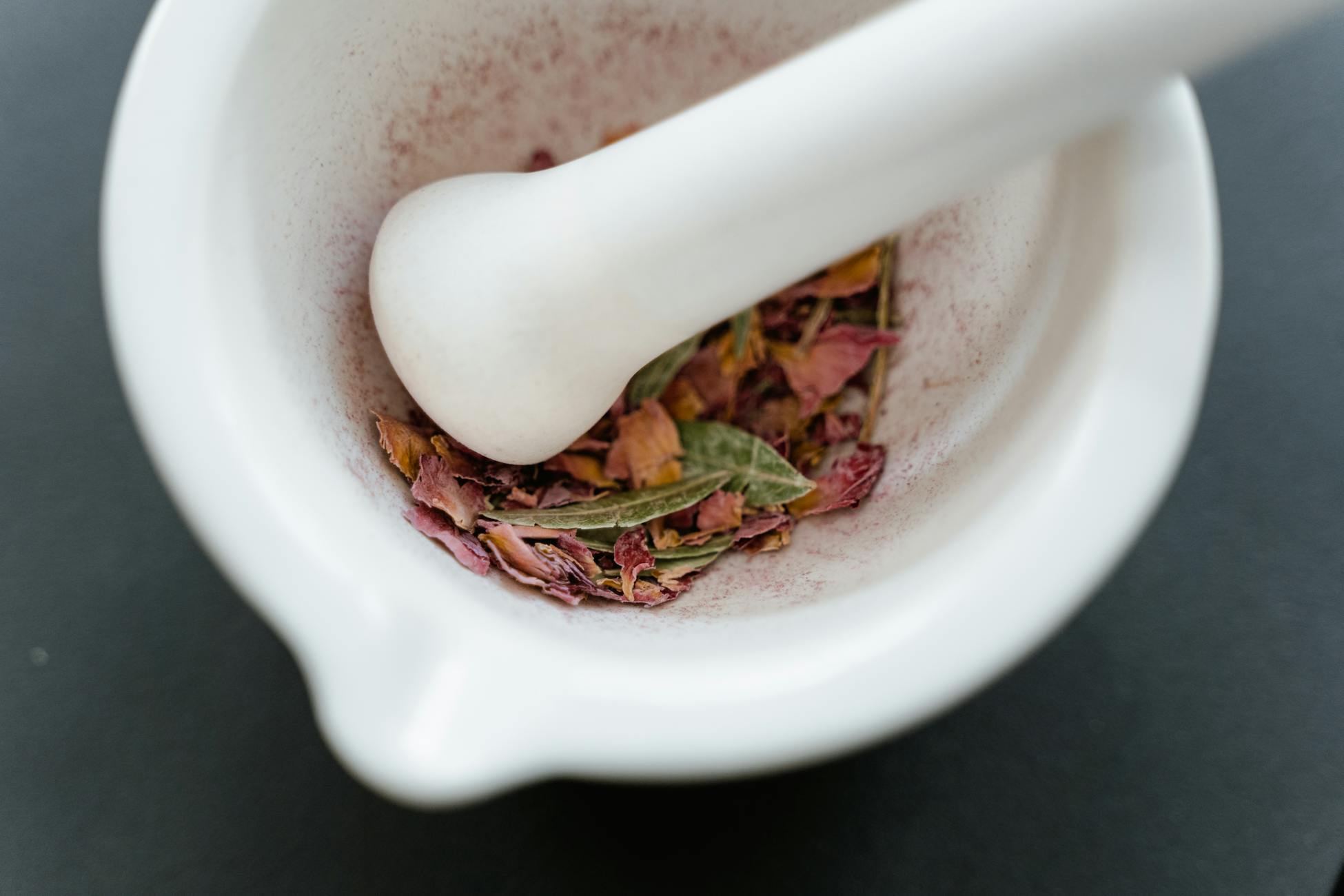 A close-up view of dried herbal petals in a white mortar and pestle, creating a fragrant and aromatic setting.