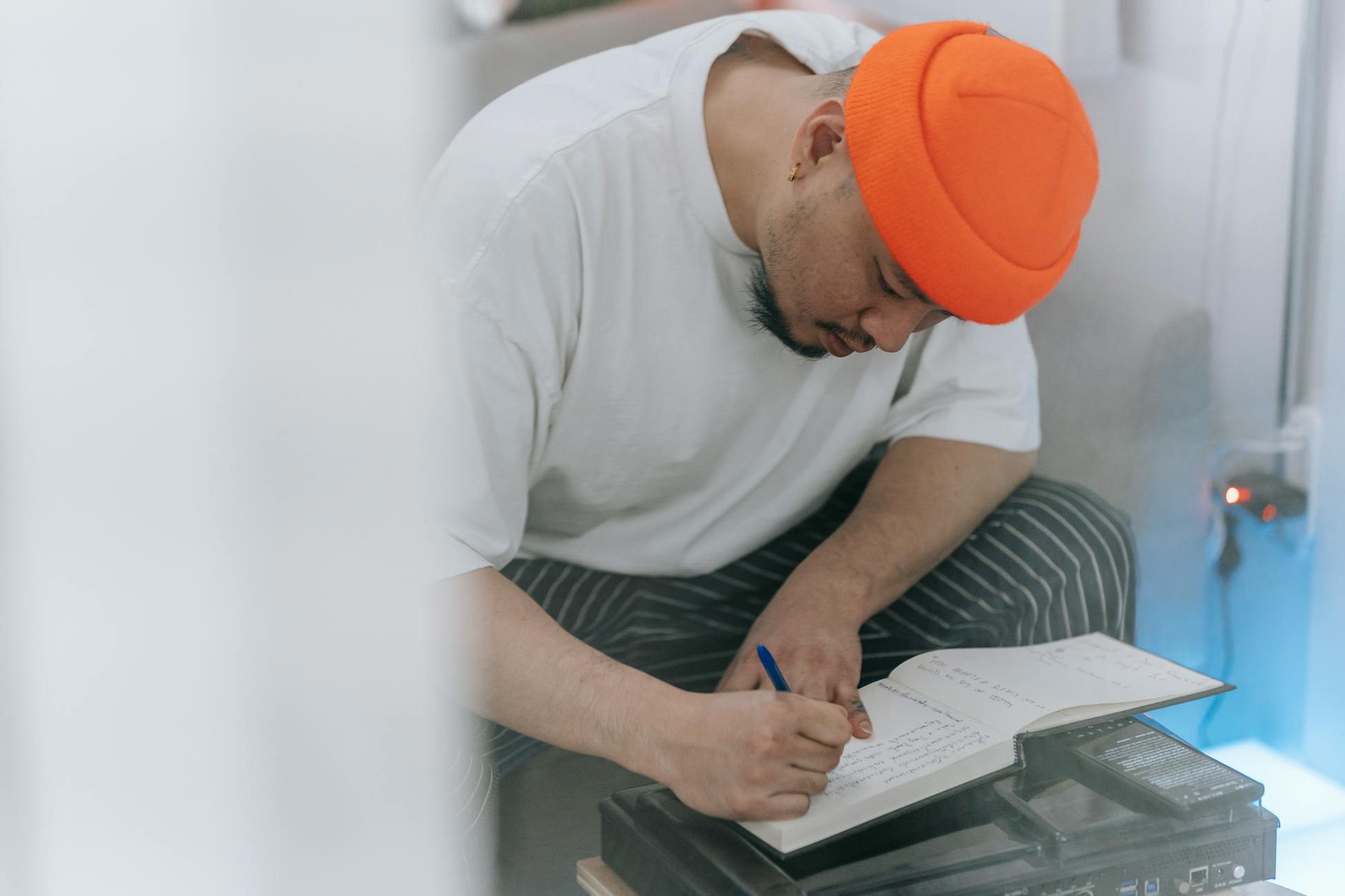 Man in an orange beanie writing in a notebook, showcasing creativity and focus.