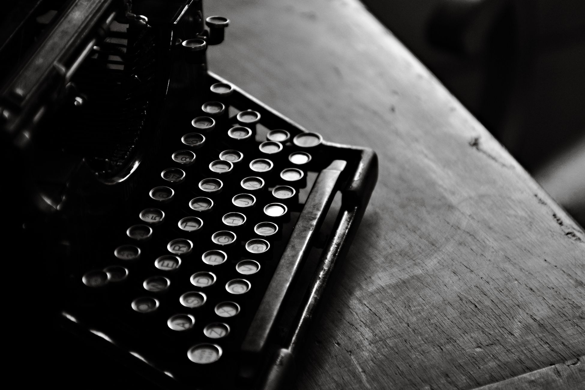 A classic black vintage typewriter in moody black and white on a wooden desk.