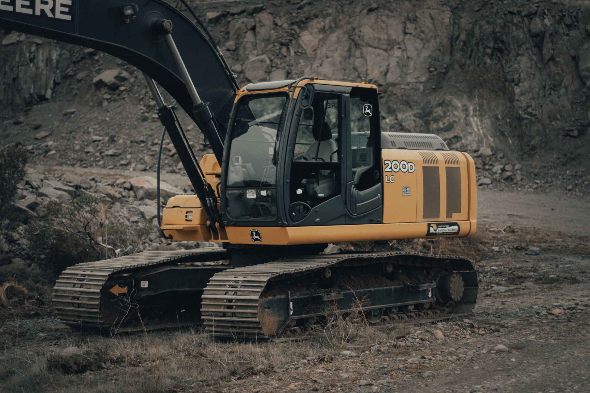 A yellow excavator operating in a rocky quarry on an overcast day.