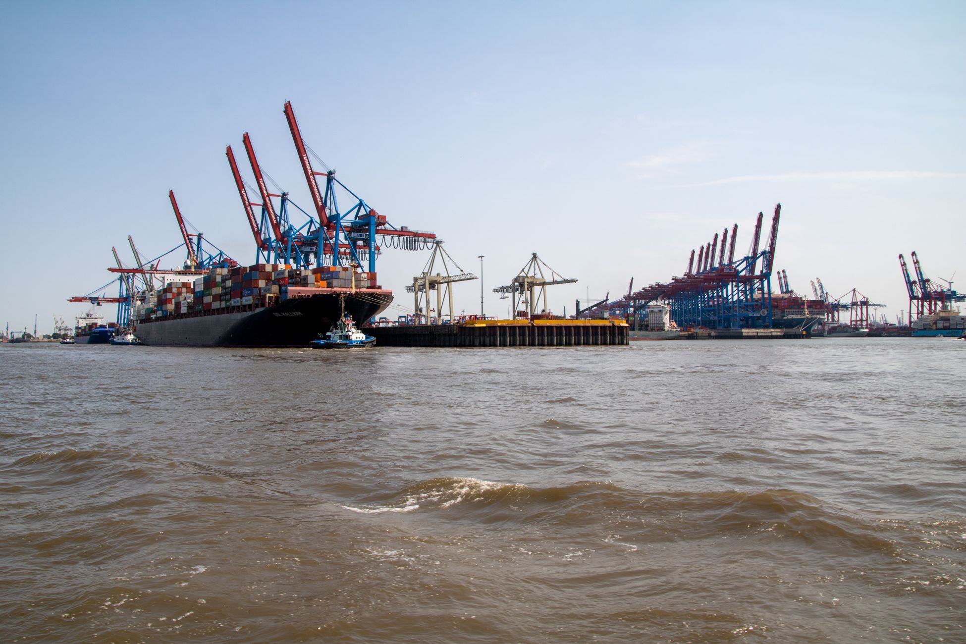 Large container ship docked at the busy Port of Hamburg with cranes in view.