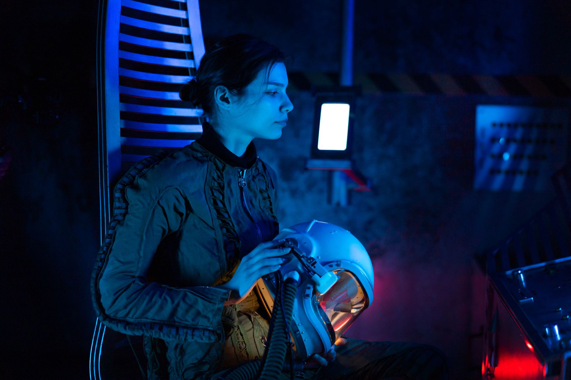 A futuristic spacewoman in a blue-lit spacecraft, holding her helmet, ready for interstellar exploration.